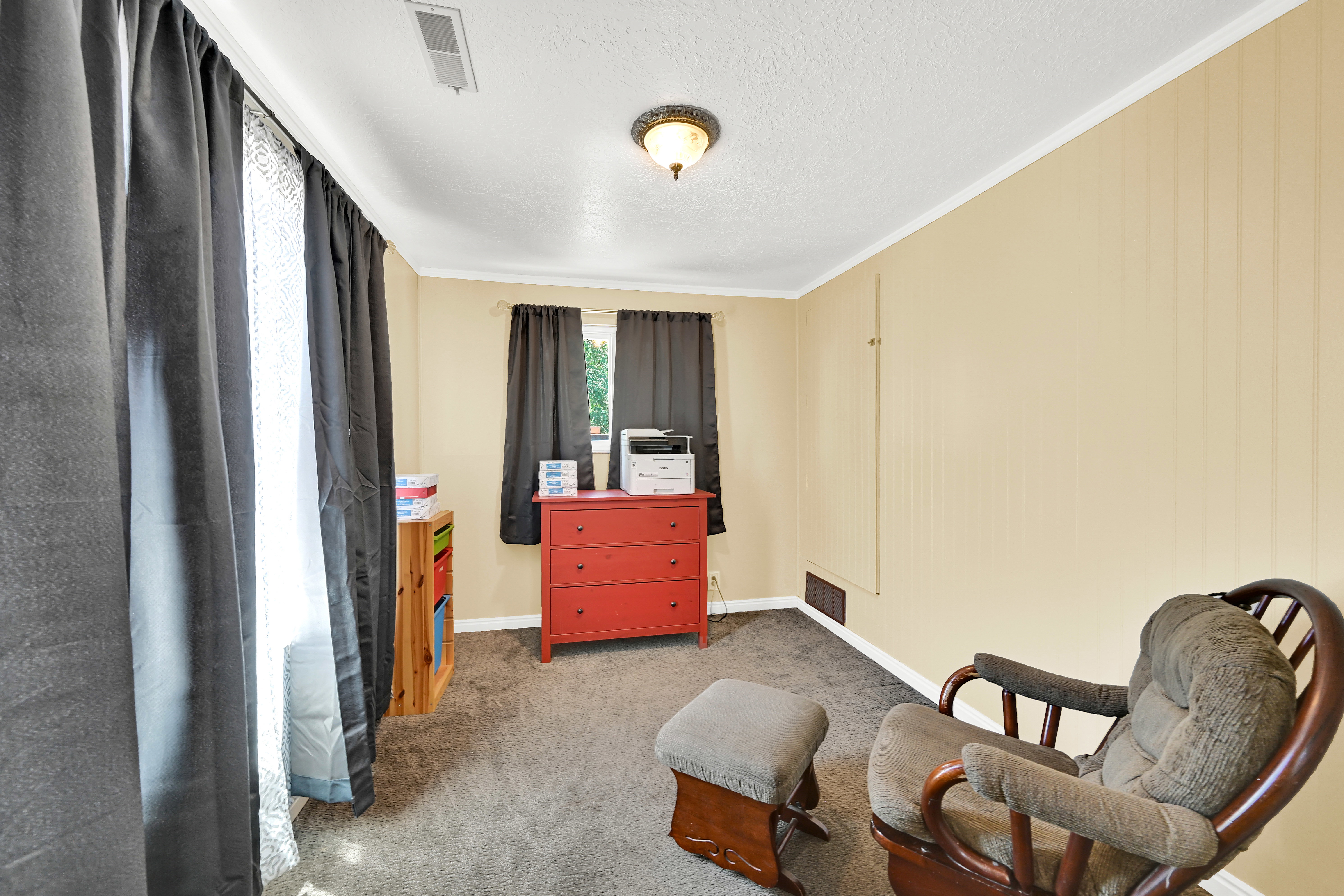 Carpeted interior room with neutral-toned walls, white crown molding, and a ceiling-mounted light fixture