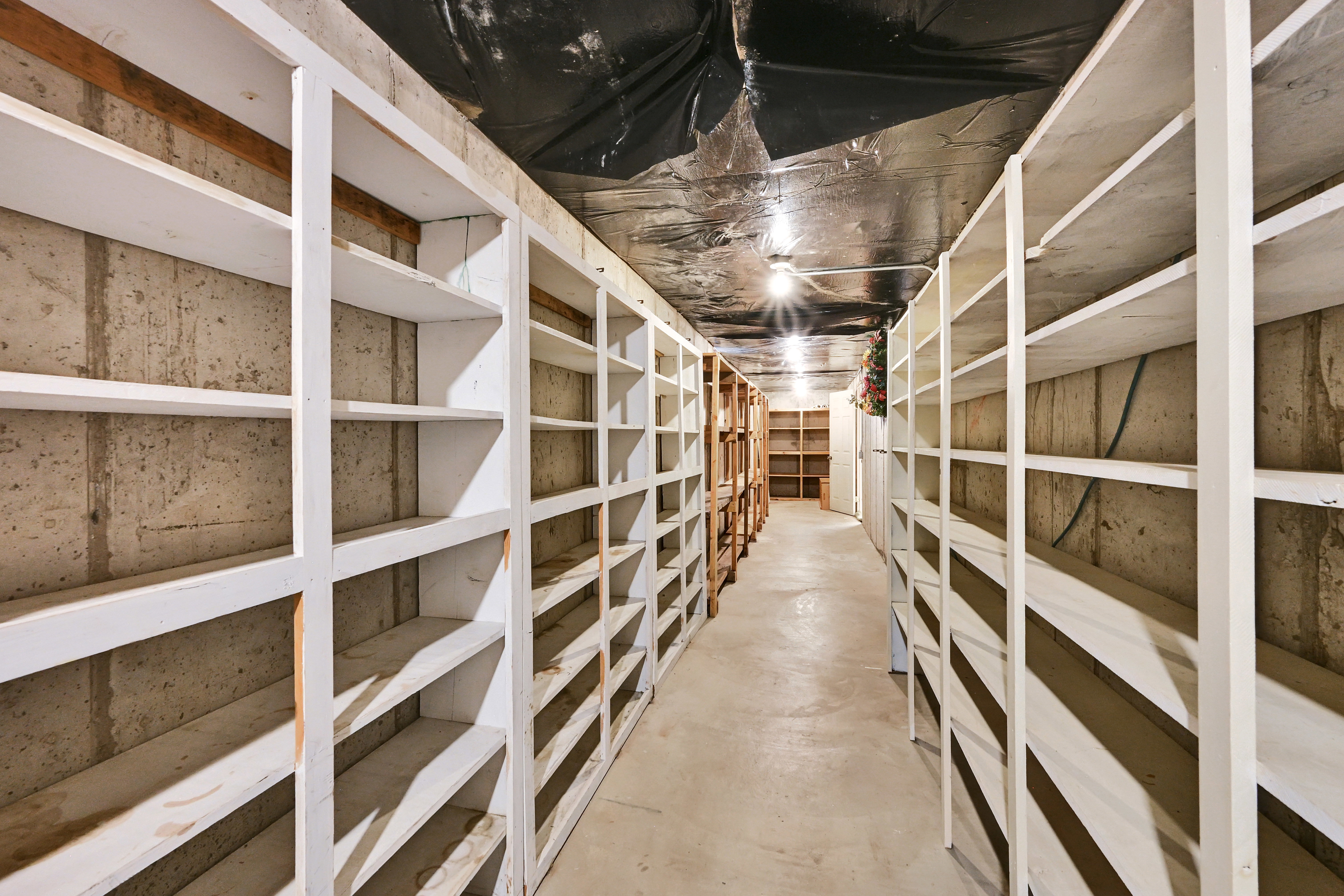 Extensive storage room featuring concrete walls, a concrete floor, and exposed ceiling joists with black sheeting