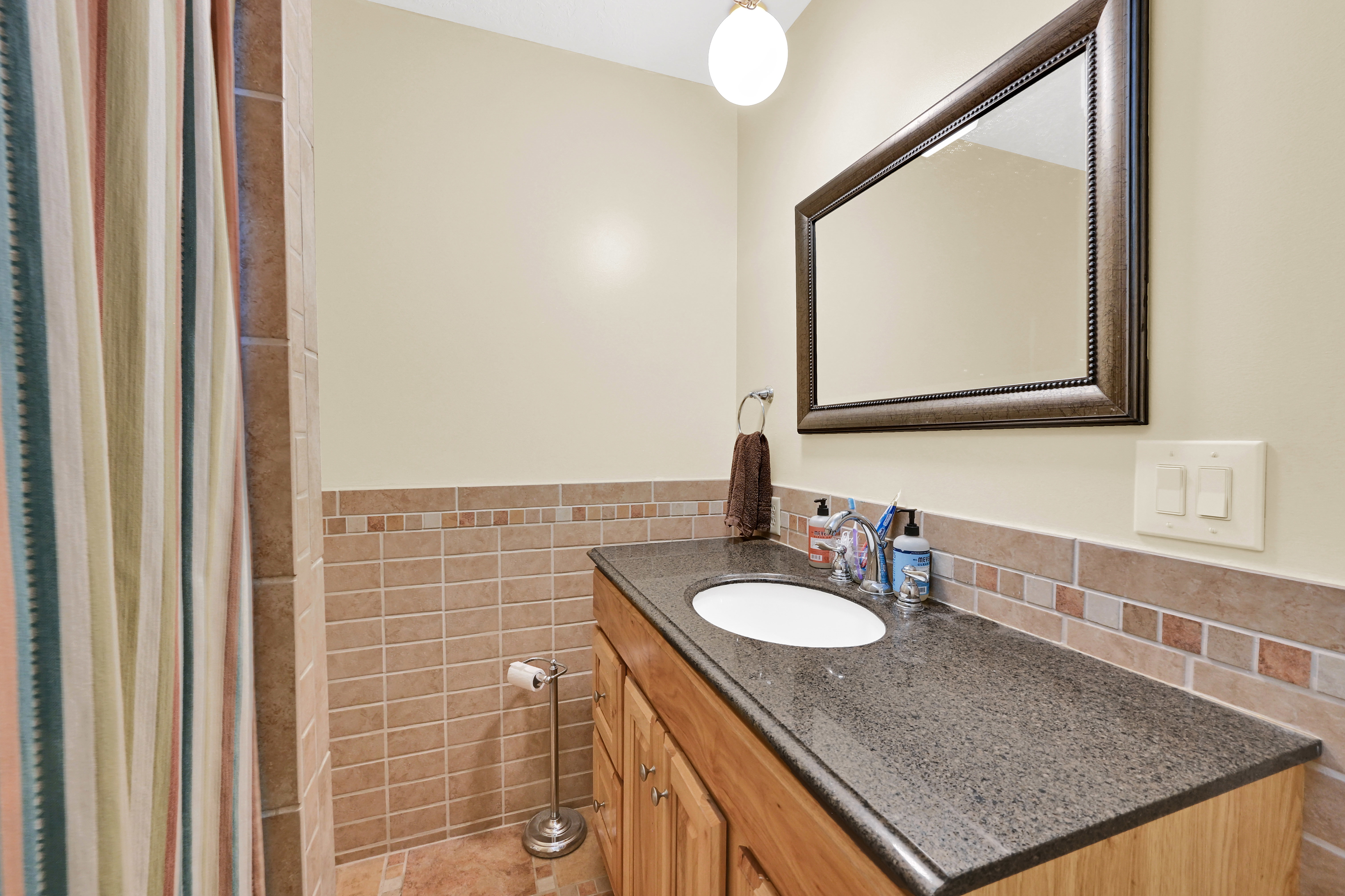 Bathroom featuring a wood vanity with an integrated sink and dark countertop, framed mirror, and tiled walls and flooring