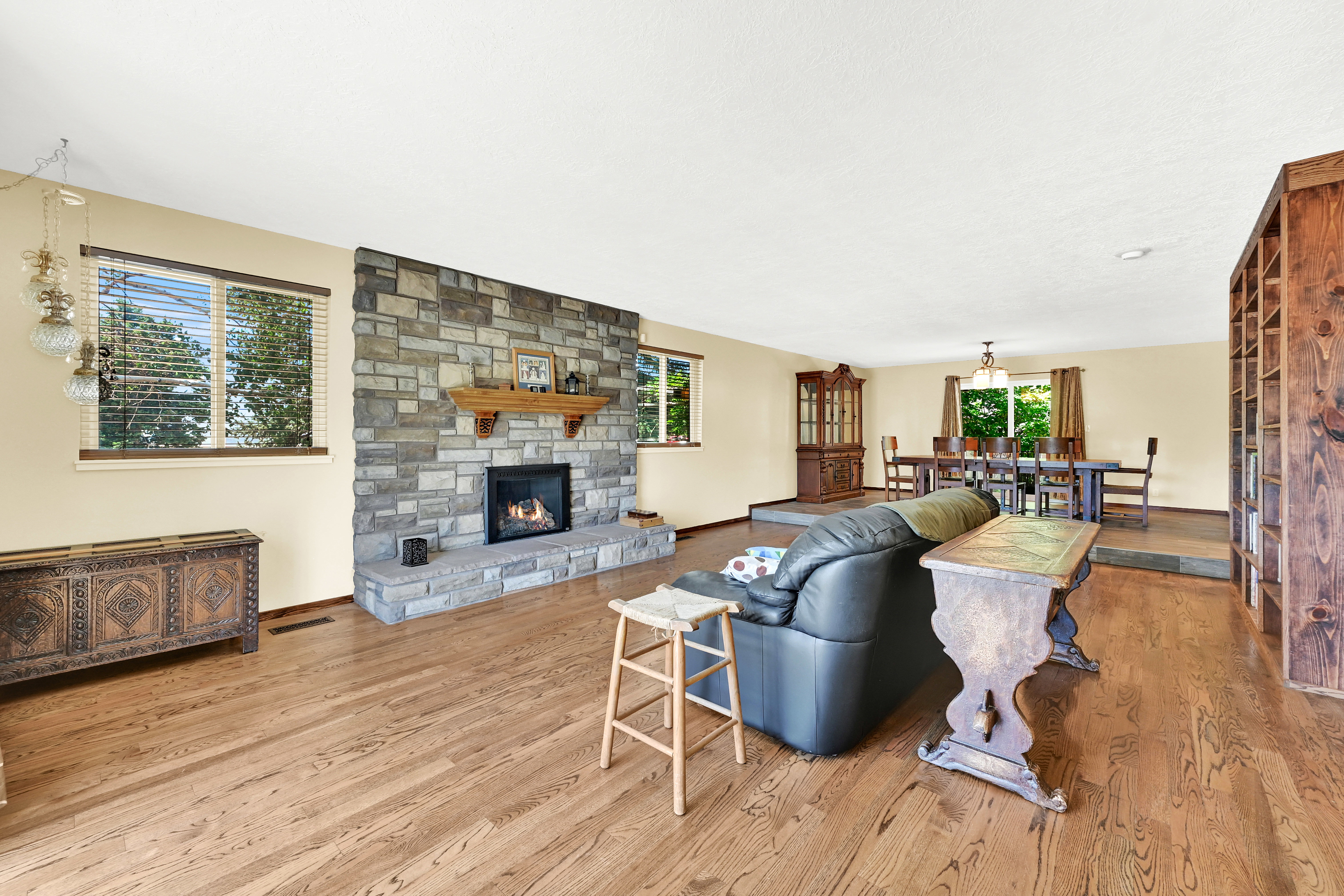 Spacious living area featuring wood-finish flooring throughout, a stone-clad fireplace with a wood mantle, and multiple windows