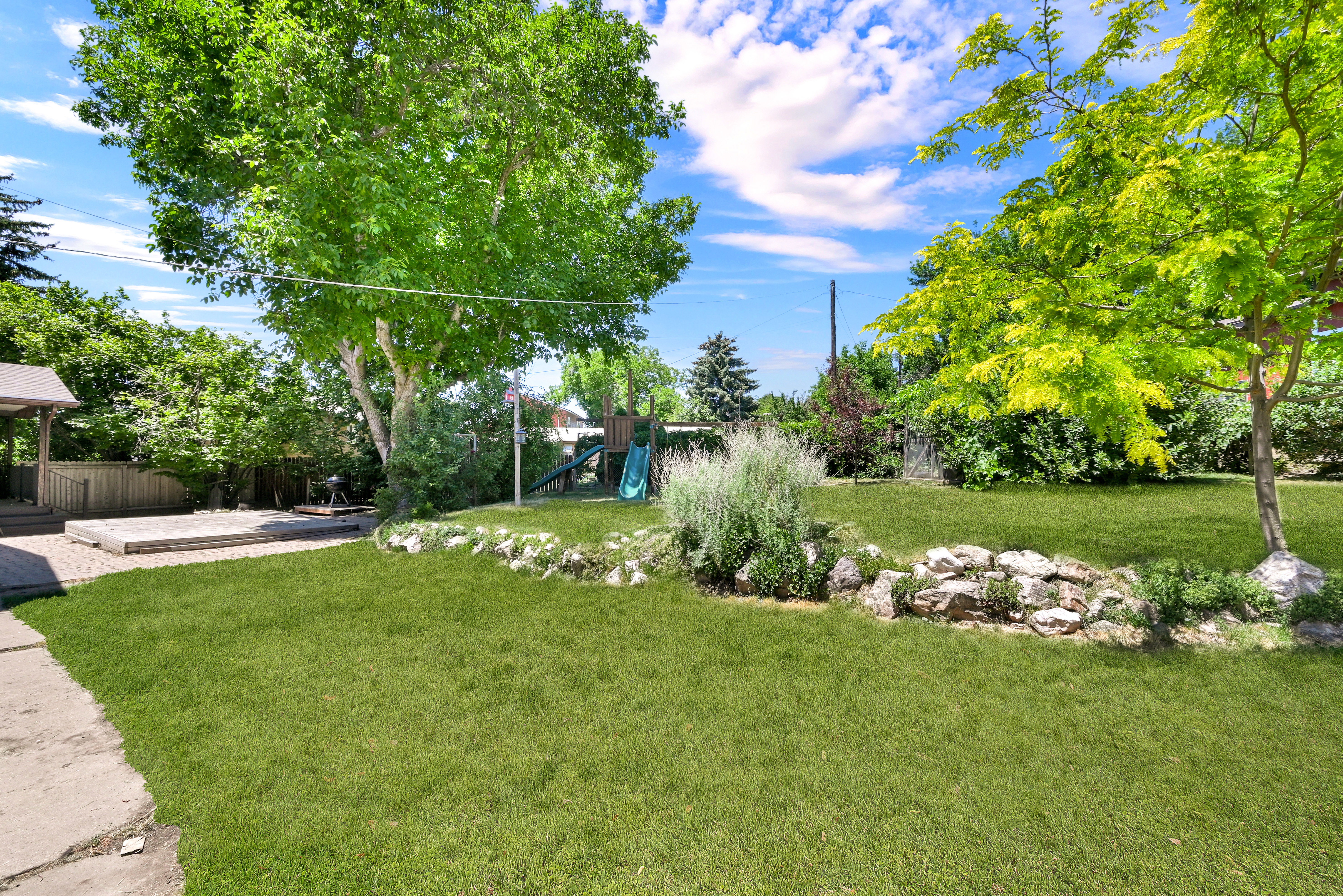 Expansive green lawn with mature trees and a stone-edged garden bed