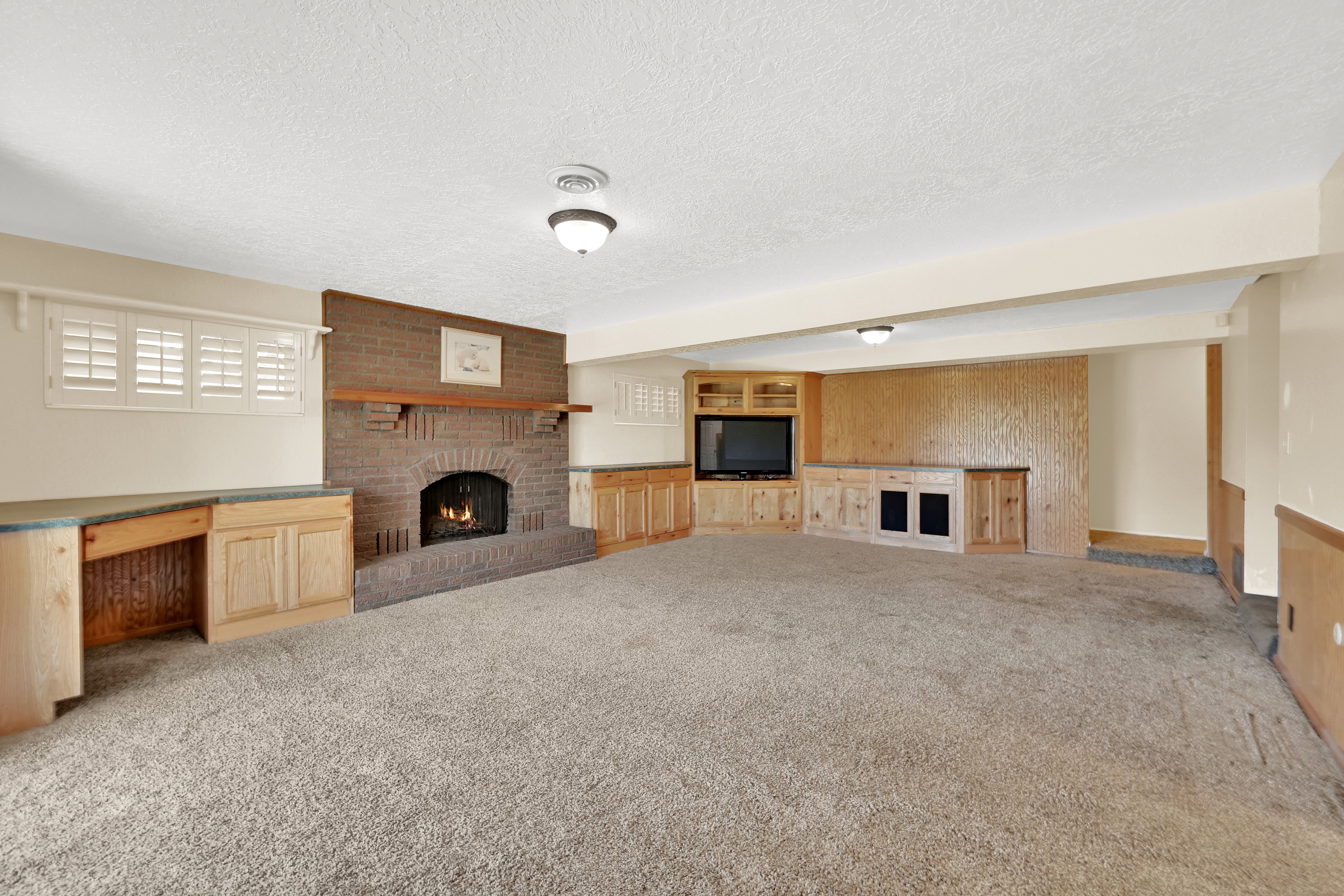 Spacious room featuring a brick fireplace with wood mantel, built-in desk with countertop, custom entertainment center, and recessed lighting fixtures