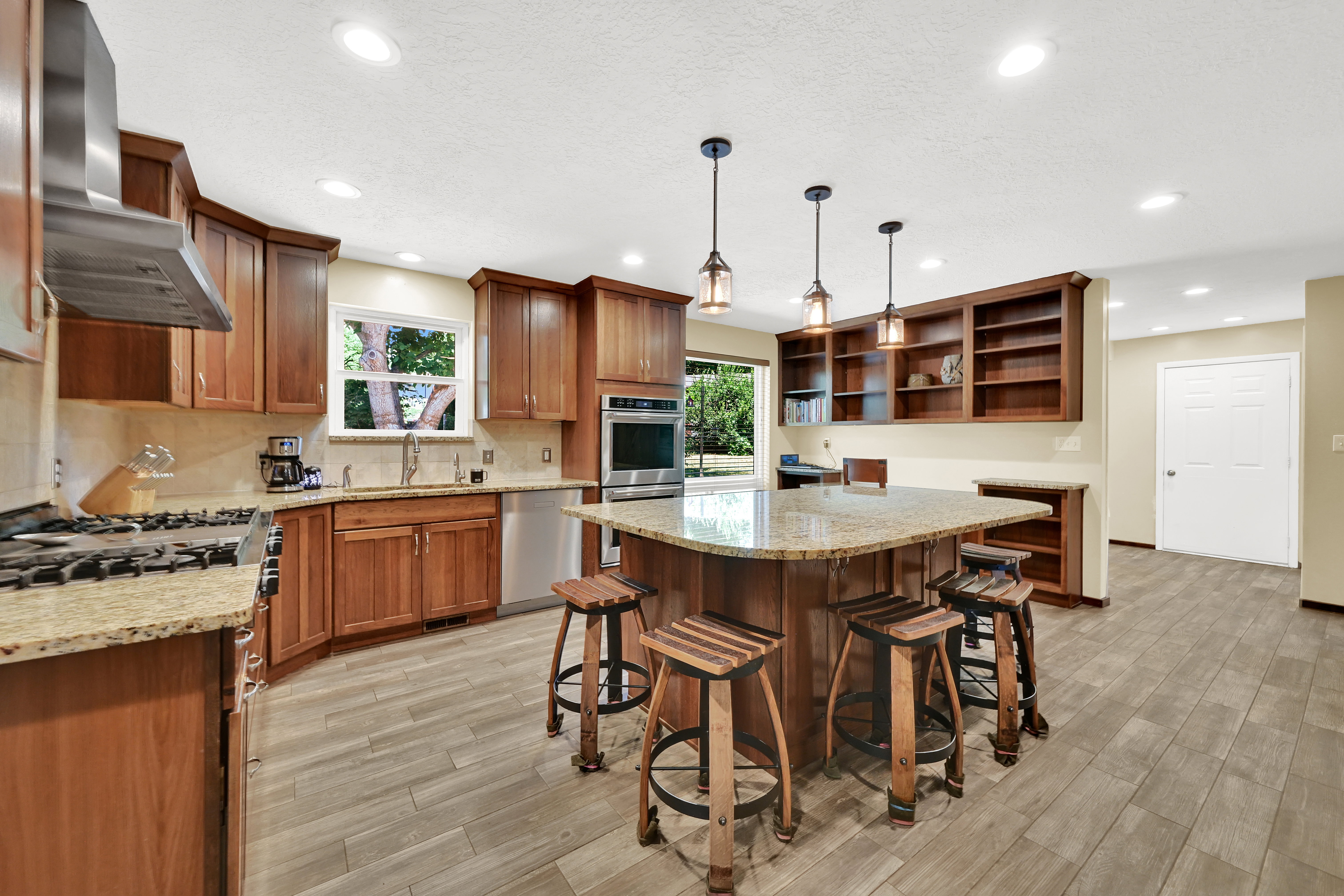 Spacious kitchen featuring an expansive island, granite countertops, wood-finish flooring, recessed lighting, and stainless steel appliances
