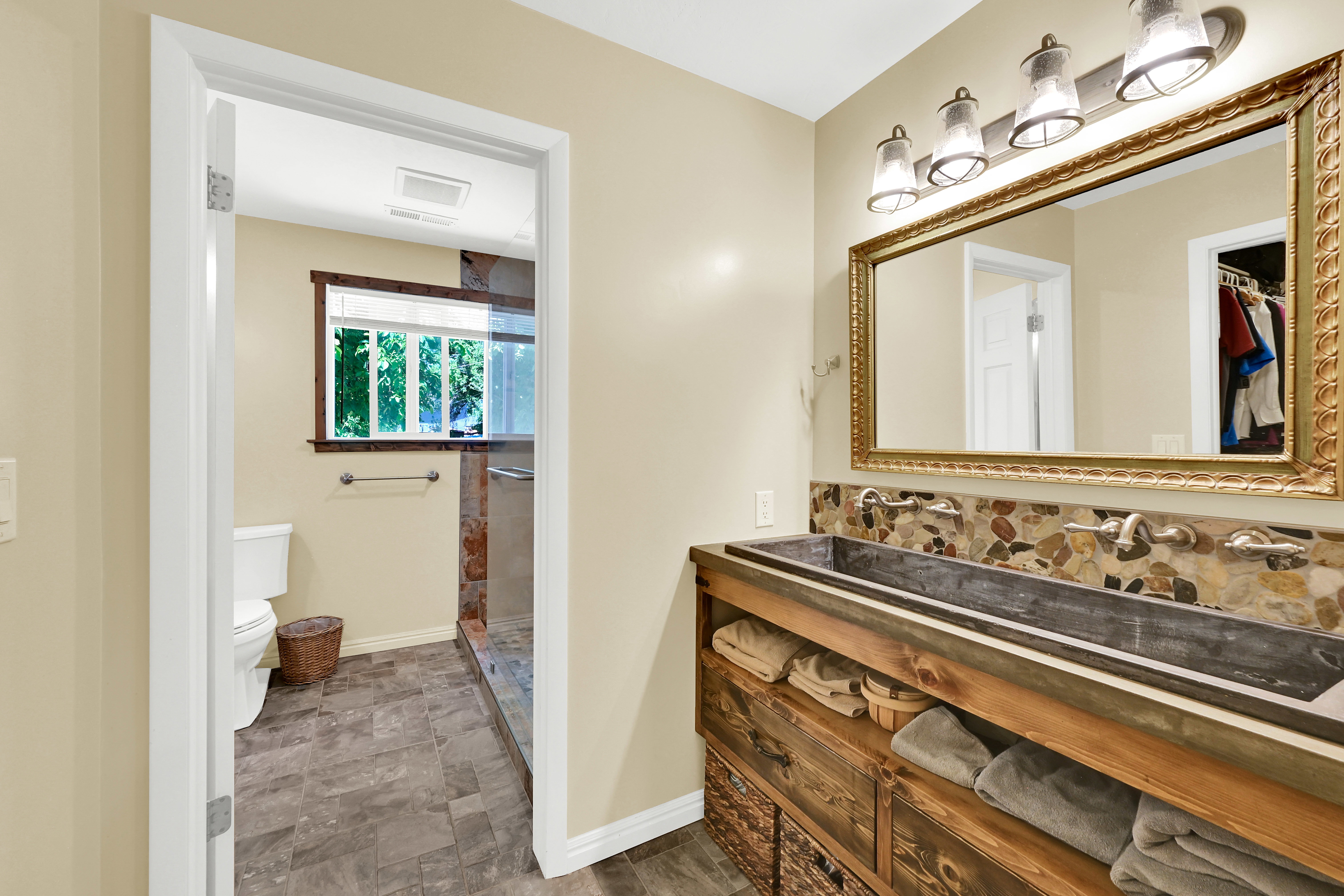 Bathroom featuring a custom double vanity with a trough sink, wall-mounted faucets, and a pebble tile backsplash