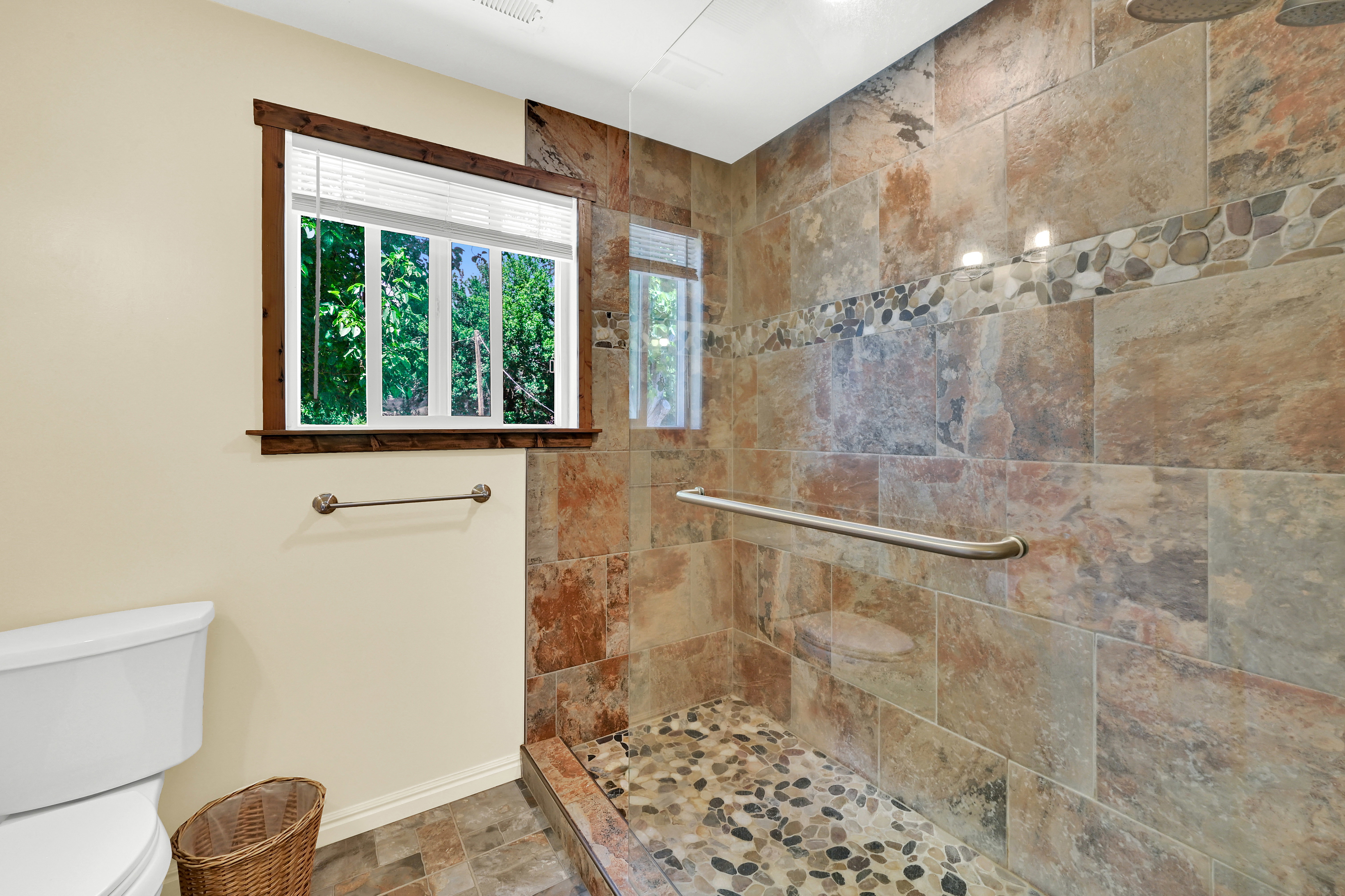 Walk-in shower featuring large format tile surrounds with a river rock accent band, a river rock shower pan, and a glass enclosure
