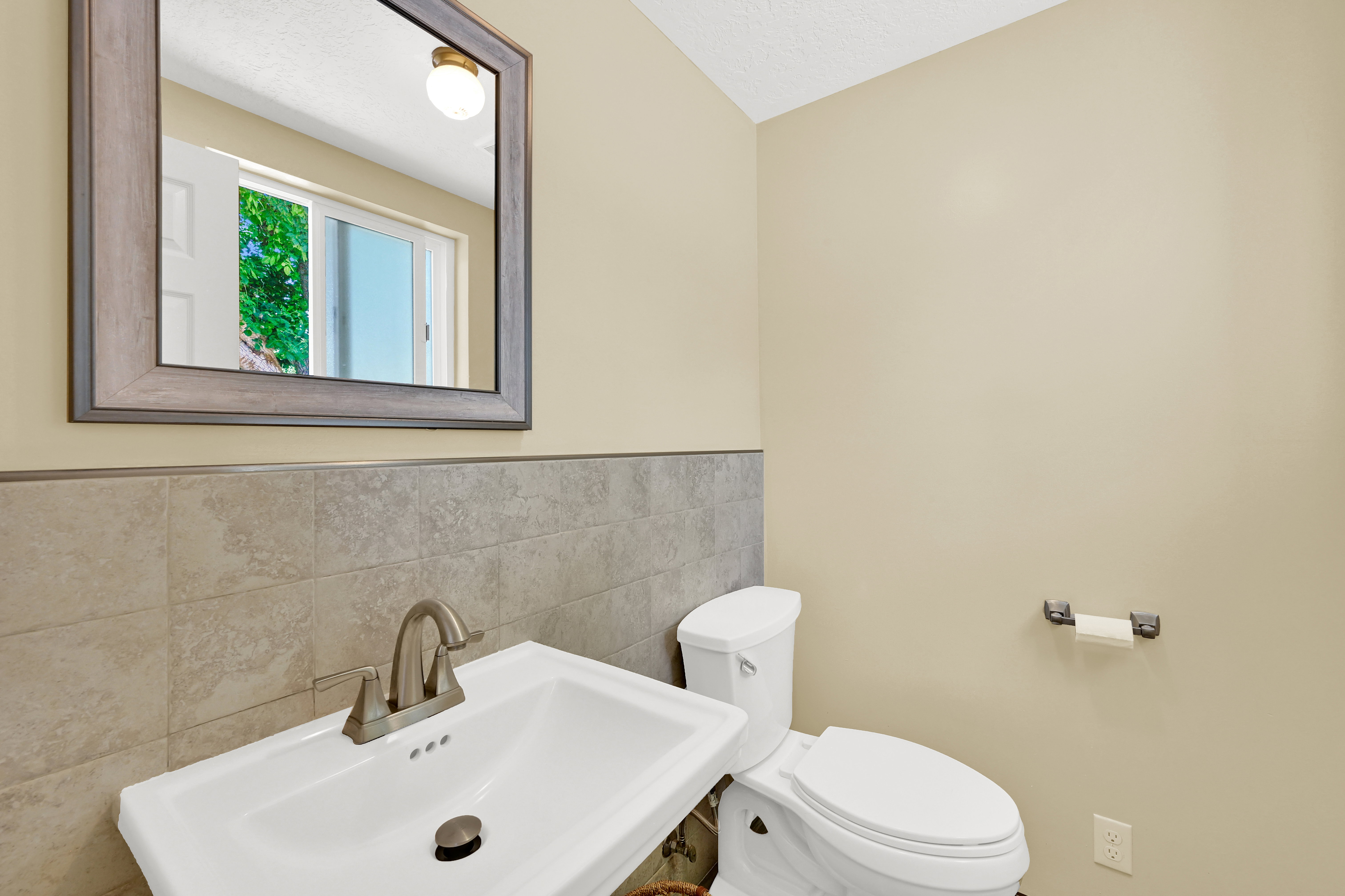 Pedestal sink with a brushed nickel faucet, complemented by a framed mirror