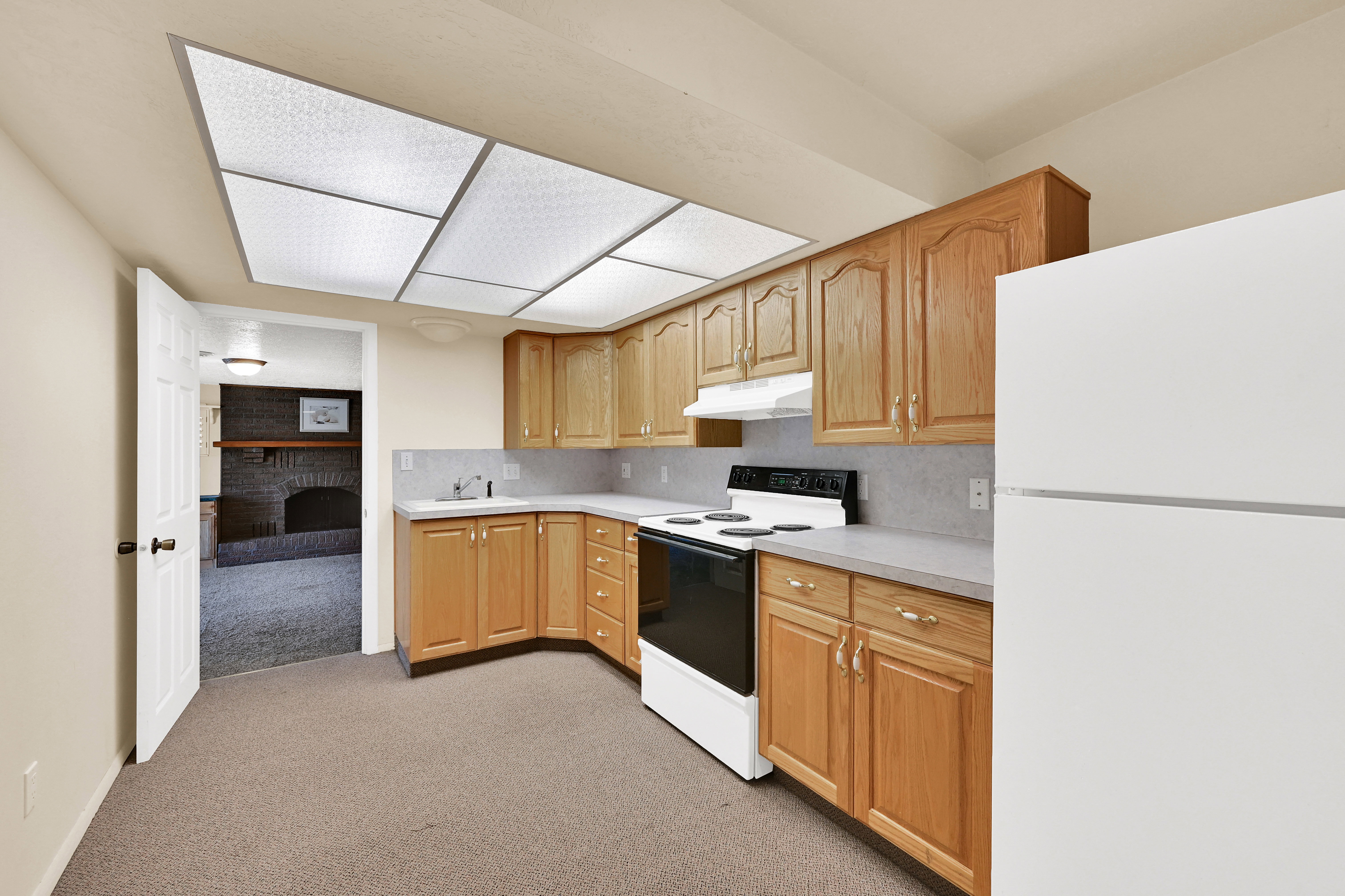 Kitchenette featuring wood cabinetry, white appliances, and a fluorescent ceiling light panel