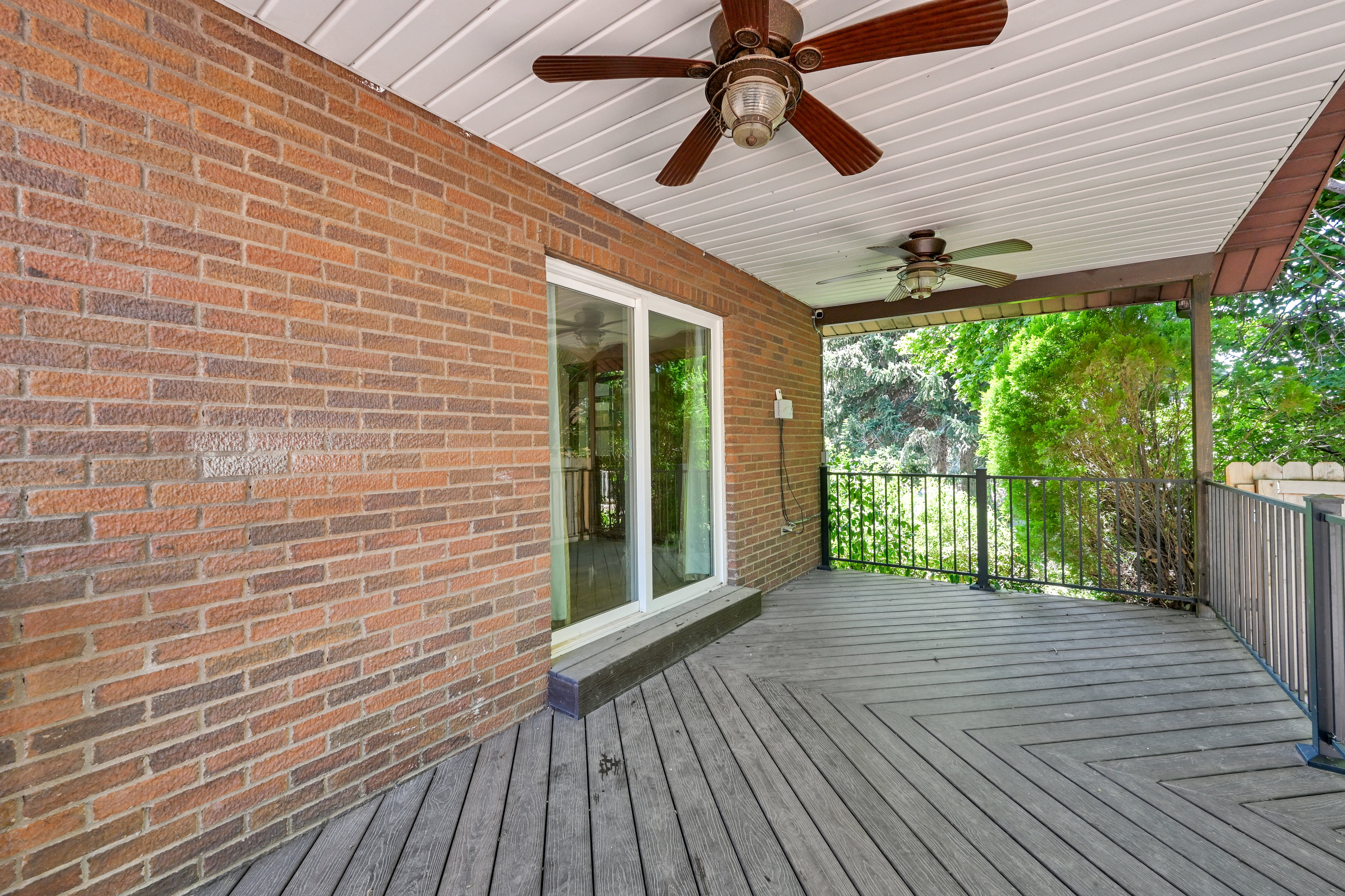 Expansive covered deck featuring wood plank flooring and a brick exterior wall