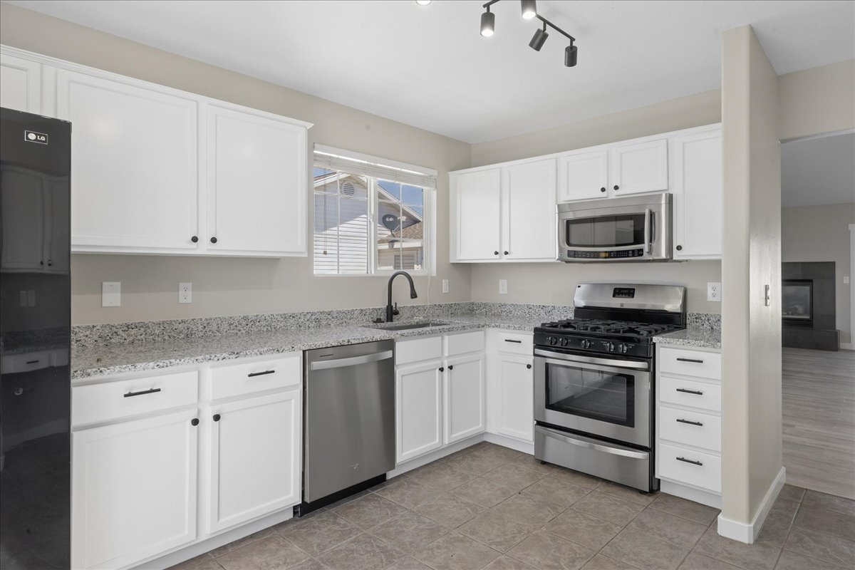 Kitchen featuring white cabinetry, speckled countertops, stainless steel appliances, and tile flooring