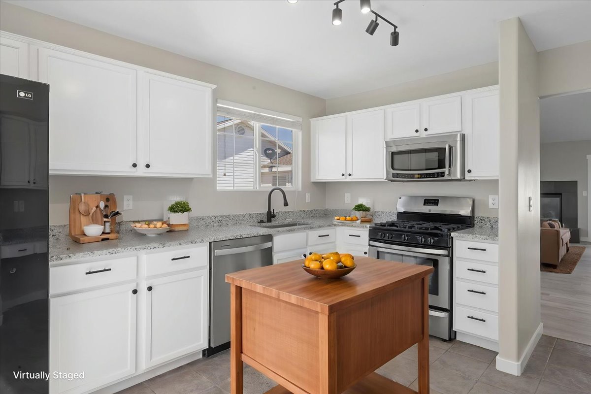 Well-appointed kitchen featuring white cabinetry, light-toned countertops, stainless steel appliances, a wood-finish island, and track lighting