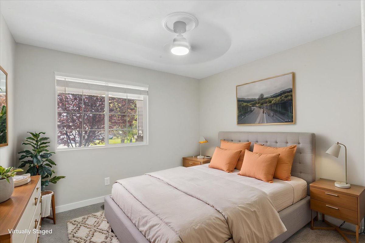 Bright bedroom featuring a large window, plush carpet flooring, a ceiling fan with integrated lighting, and a neutral color palette