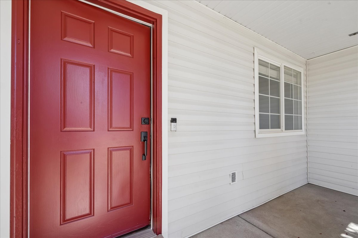 Red paneled entry door with black hardware, white vinyl siding, and a multi-pane window