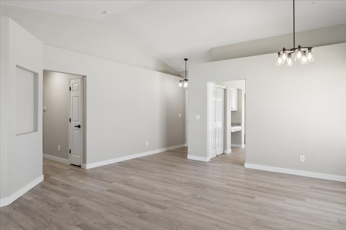 Spacious interior featuring wood-finish flooring, vaulted ceilings, modern black chandeliers, and white baseboards