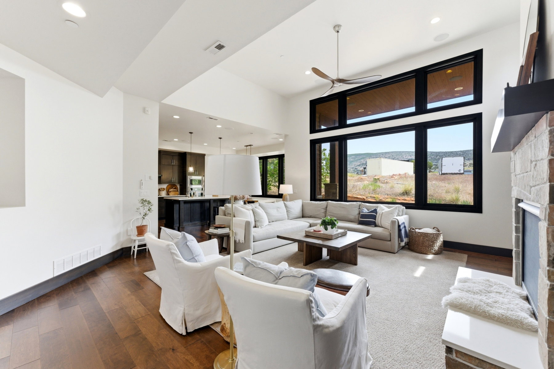 Spacious living area featuring large black-framed windows, wood-finish flooring, a stone-faced fireplace, a ceiling fan, and recessed lighting
