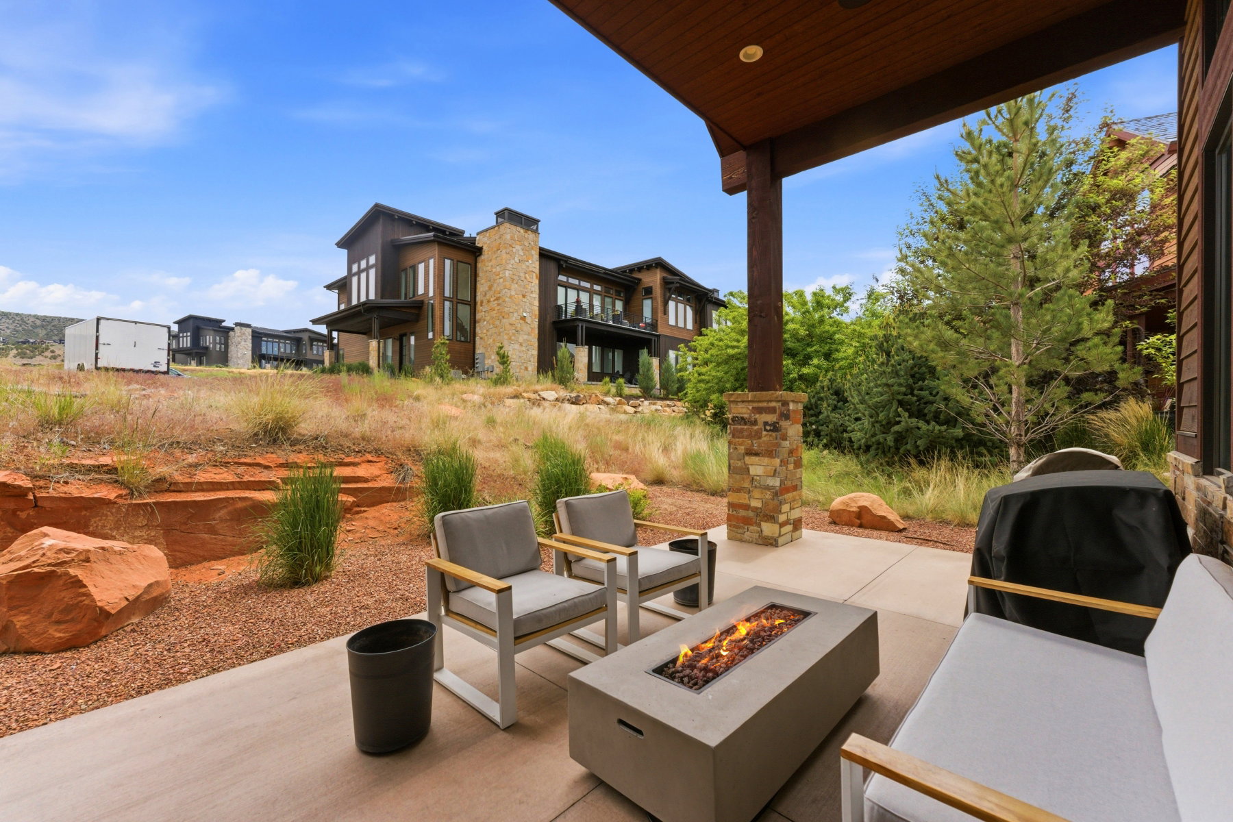 Expansive covered patio featuring a built-in fire pit, concrete flooring, and stone-clad support pillars