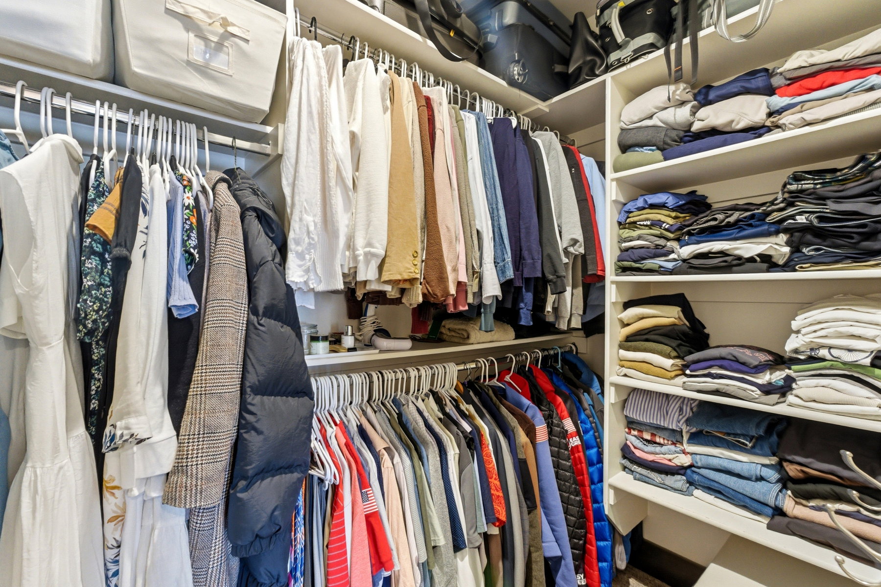 Custom closet system featuring multiple hanging rods, integrated shelving, white wood-finish construction, and upper storage compartments