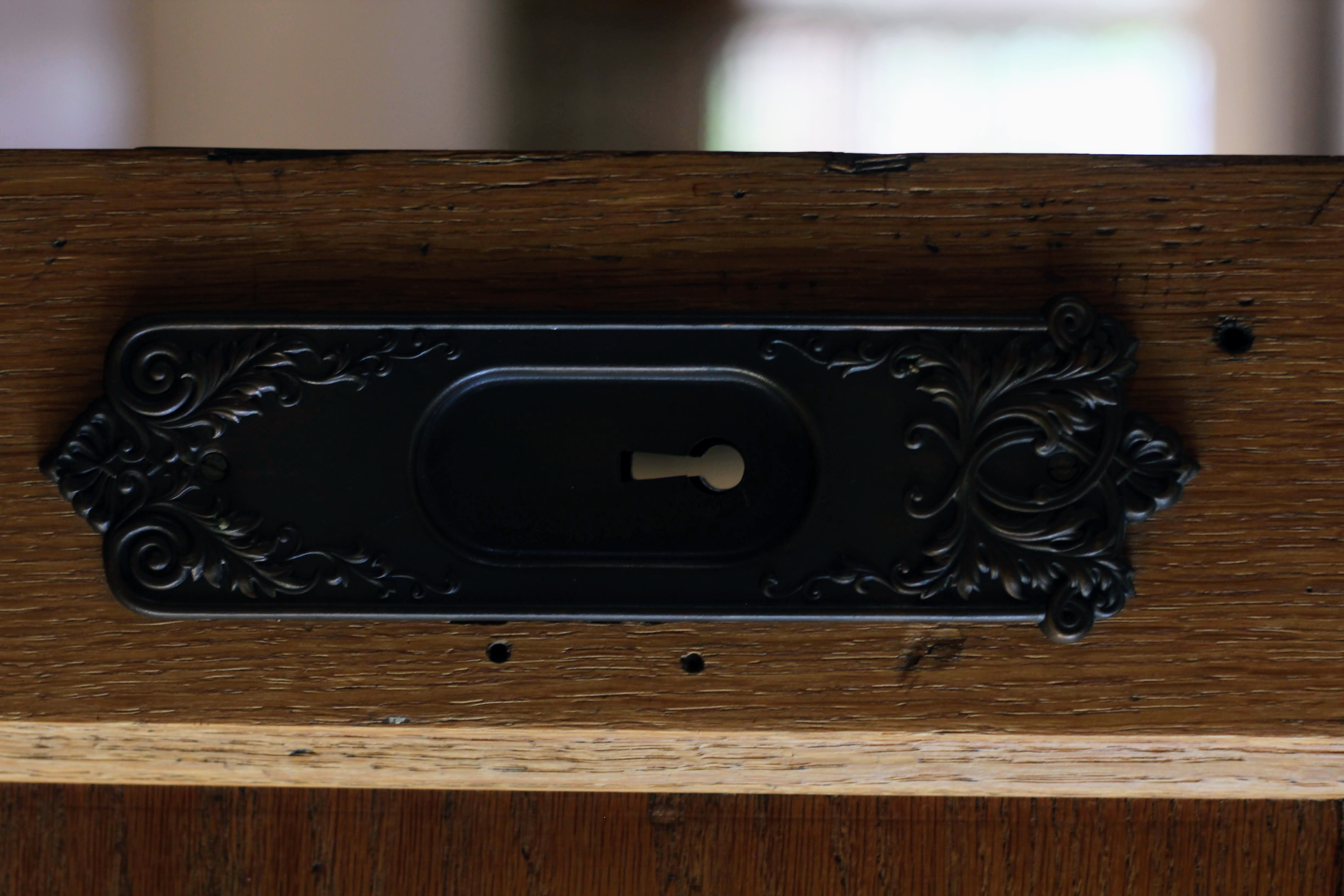 Ornate dark-finish escutcheon plate with a keyhole, set against a rich wood door frame