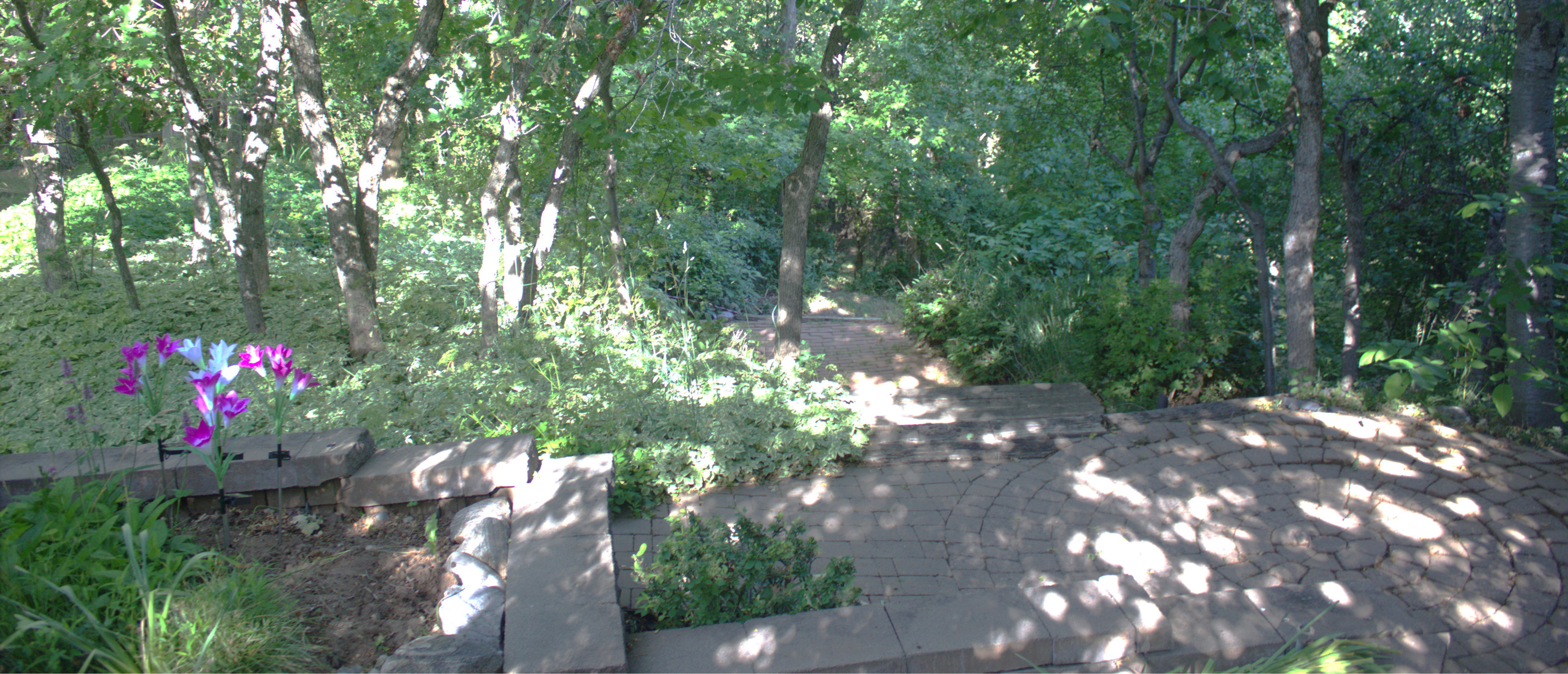 Tiered landscaping with natural stone pavers, a planting bed, and mature trees providing natural shading