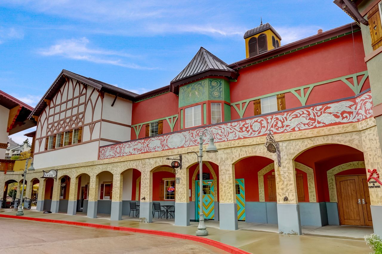 Multi-story commercial building featuring a vibrant red facade with decorative green trim, arched ground-level entryways, and a distinct half-timbered section