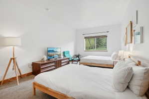 Spacious room featuring two platform beds, a large window with exterior greenery, and wood-finish flooring