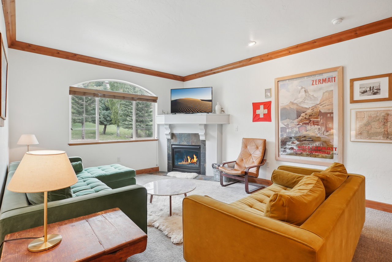 Living area featuring wood beam ceiling accents, a large arched window, and a stone fireplace with a built-in hearth