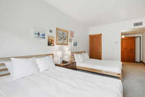 Bedroom featuring two platform beds, wood-finish interior doors, and neutral carpeting