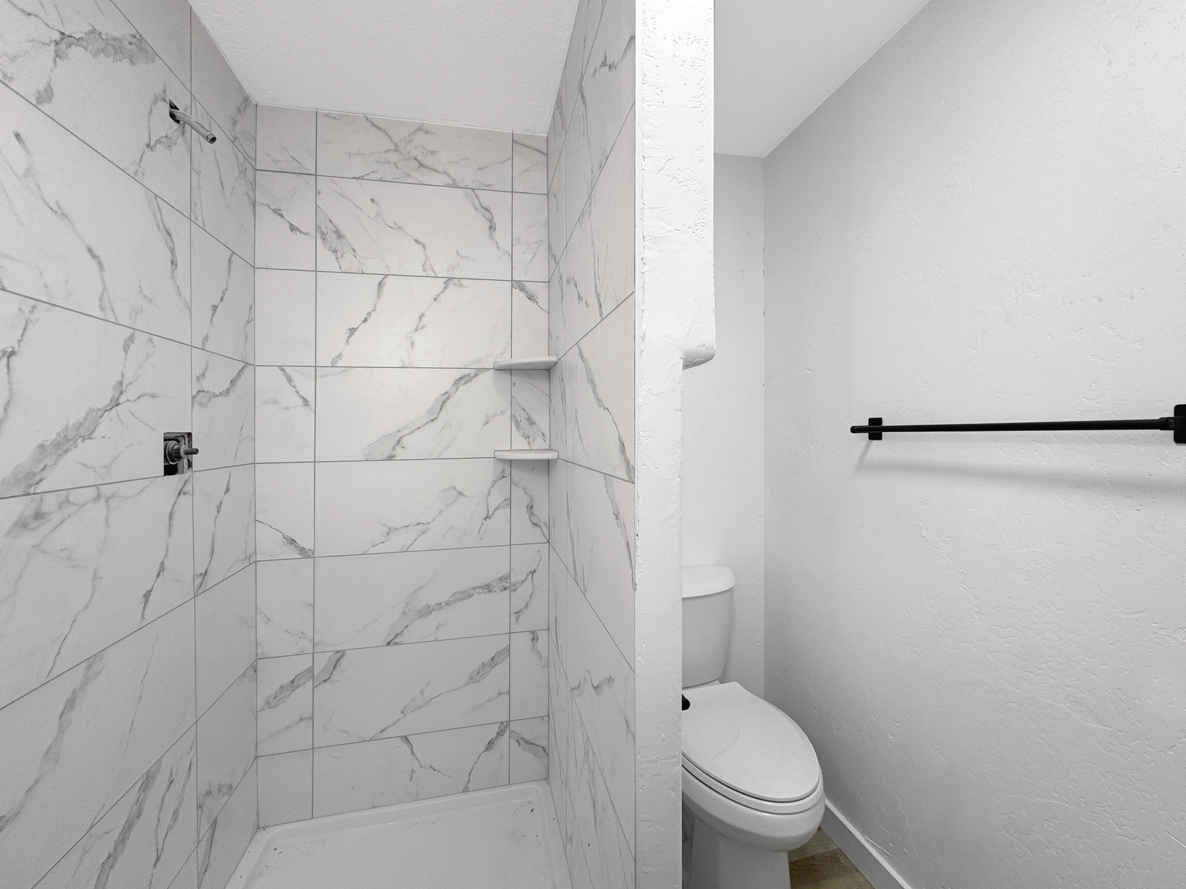 Walk-in shower with large format, marbled tile walls, integrated shelving, and a chrome shower fixture