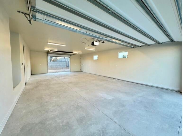 Spacious garage featuring a concrete floor, overhead lighting, and two small windows for natural light