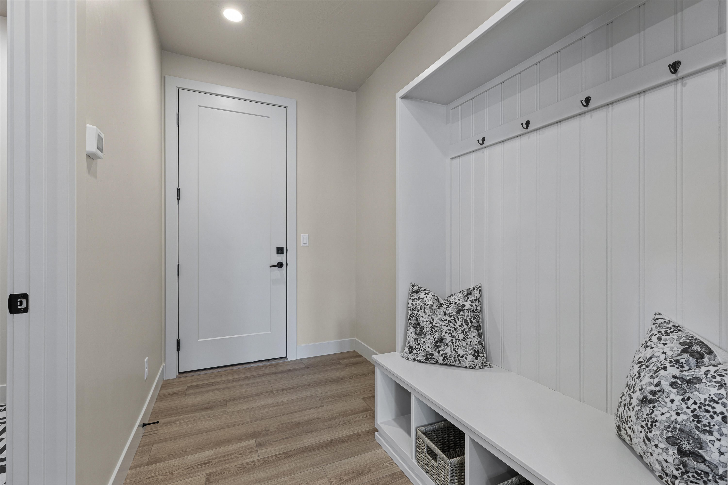 Entryway mudroom featuring wood-finish flooring, a built-in bench with open storage cubbies, beadboard paneling, and matte black coat hooks