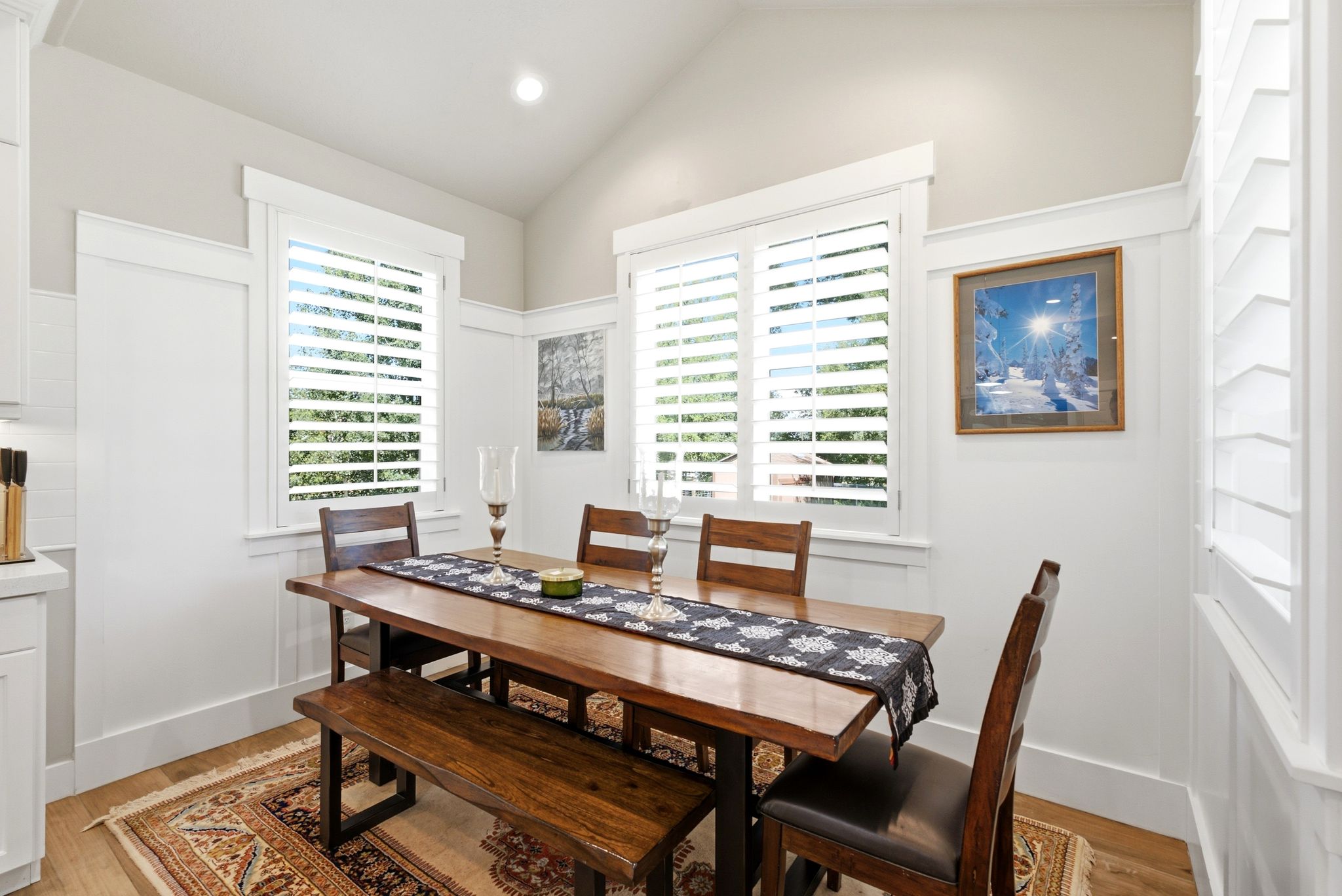 Vaulted ceiling with recessed lighting, white board and batten wainscoting, wood-finish flooring, and white plantation shutters on multiple windows