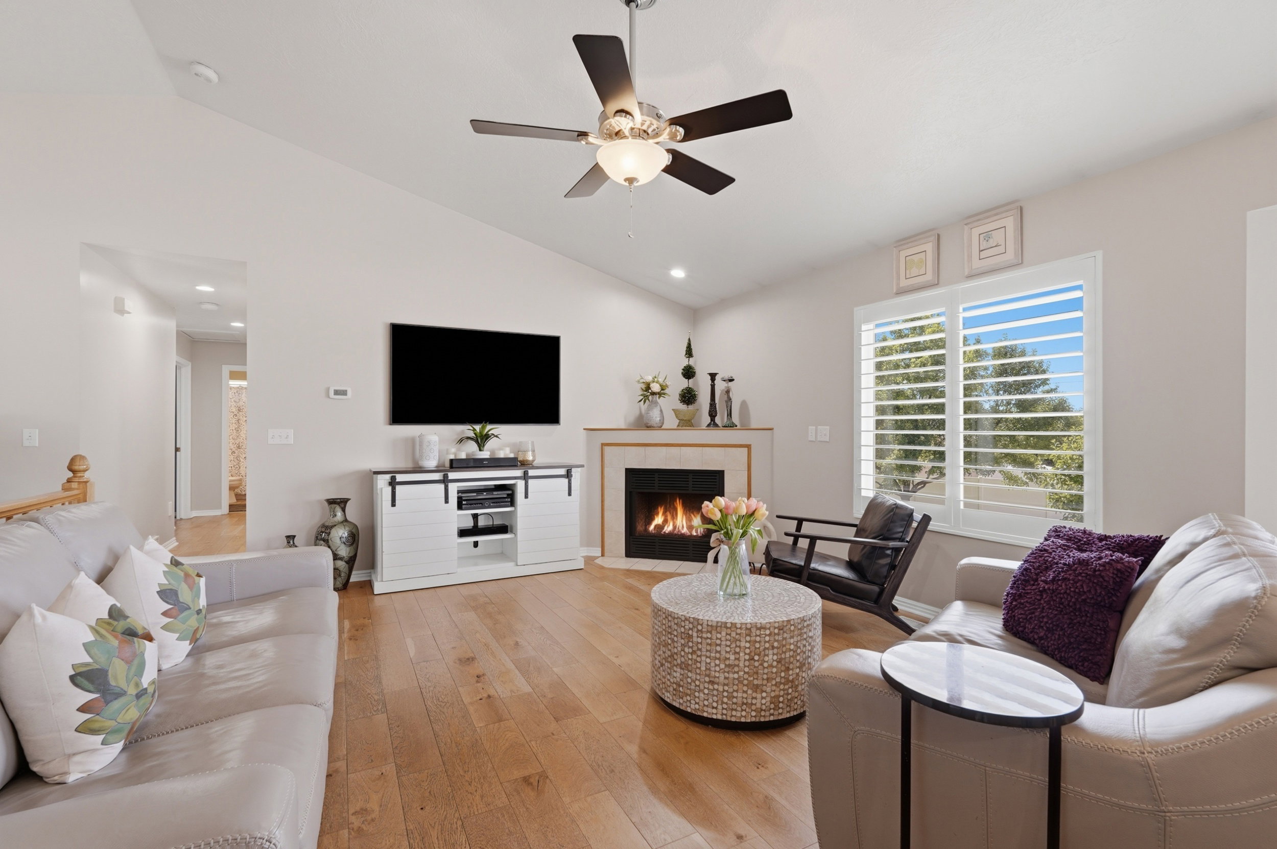 Spacious living area featuring high vaulted ceilings, light wood-finish flooring, and a corner fireplace with a stone surround