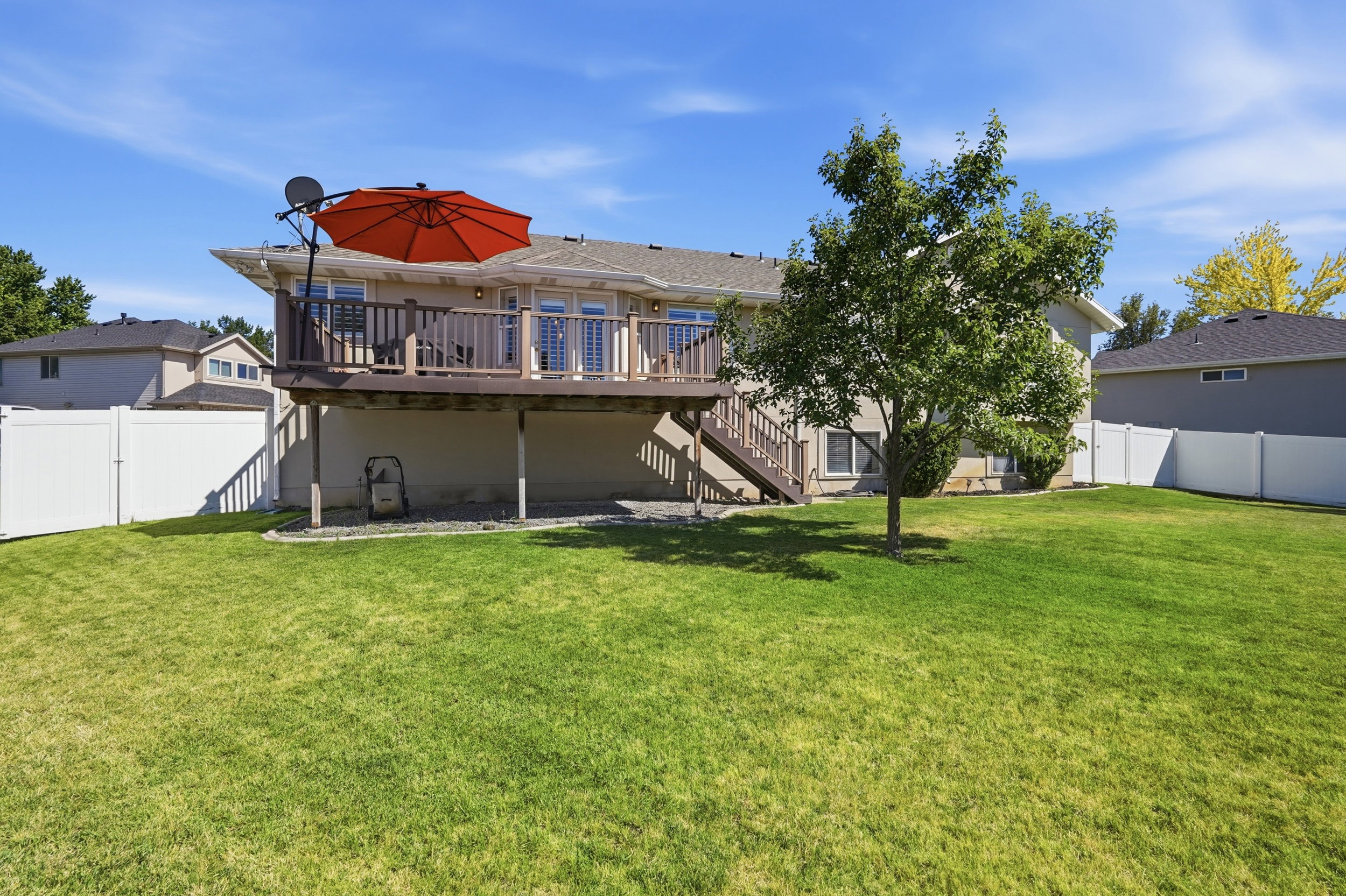 Expansive green lawn with a mature tree, featuring a raised outdoor deck with wooden railings and stairs