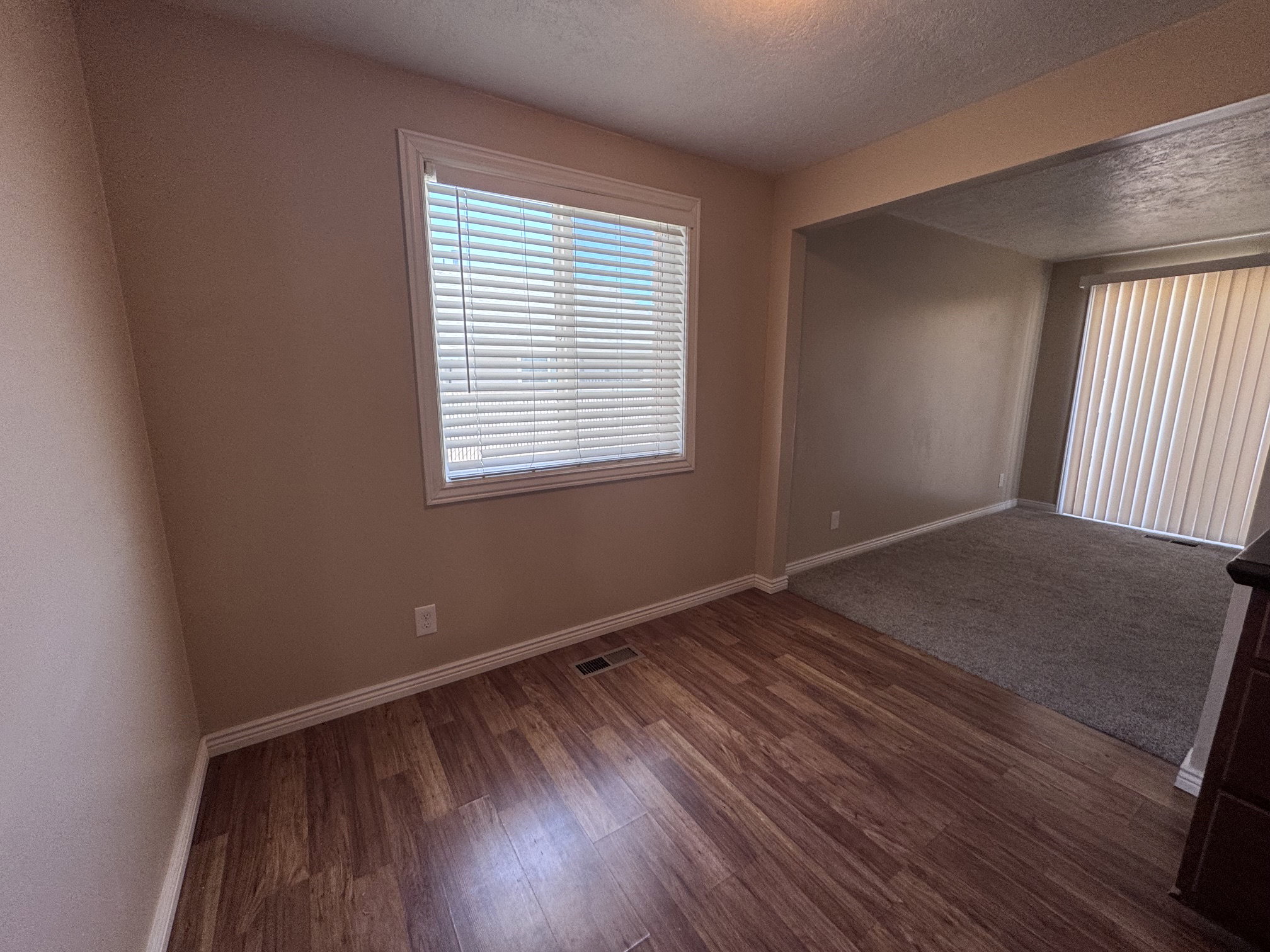 Wood-finish flooring in a neutral-toned room with a window featuring white blinds