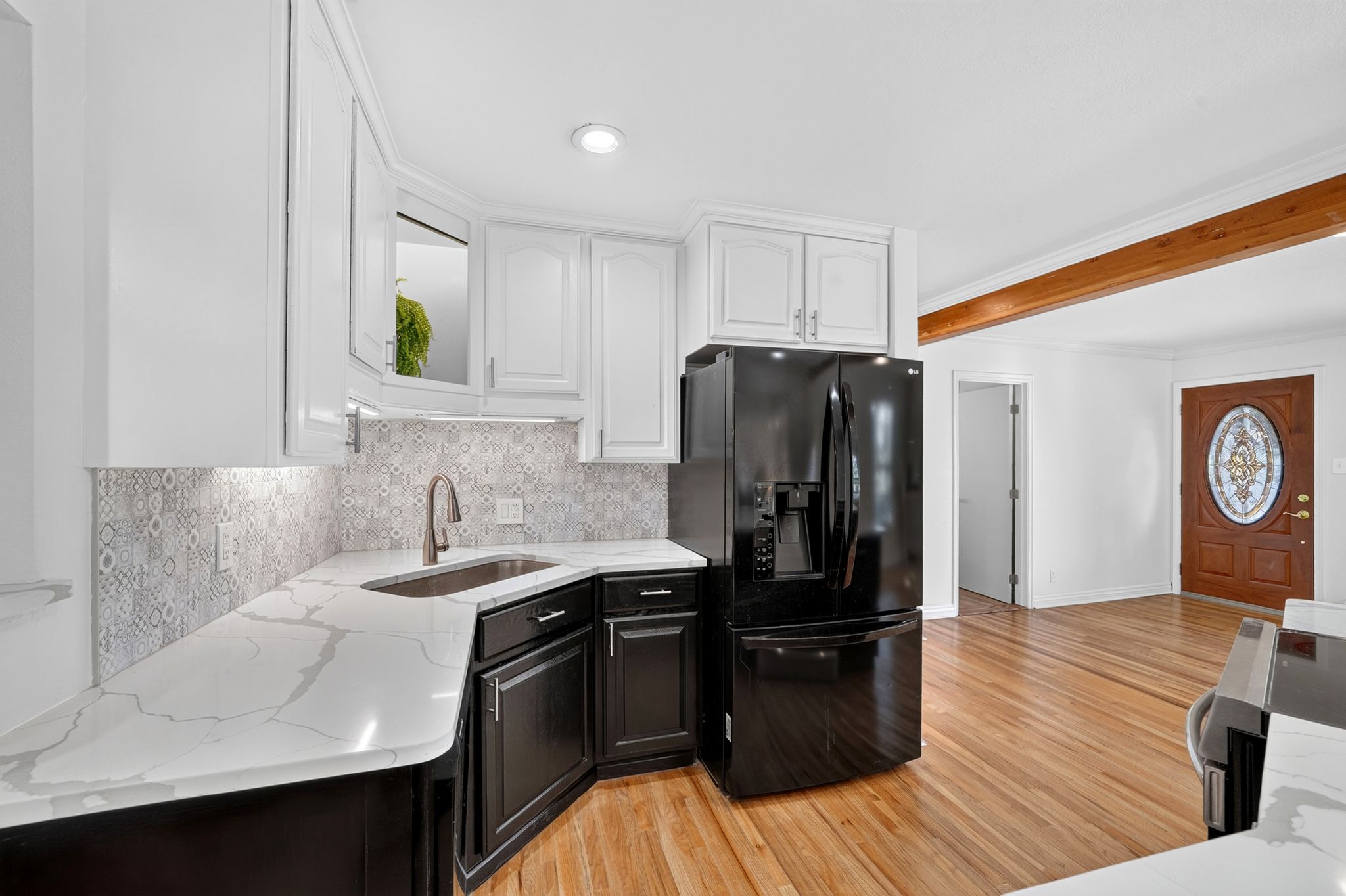 Kitchen featuring white upper cabinetry, dark lower cabinetry, patterned tile backsplash, and light-toned countertops with veining