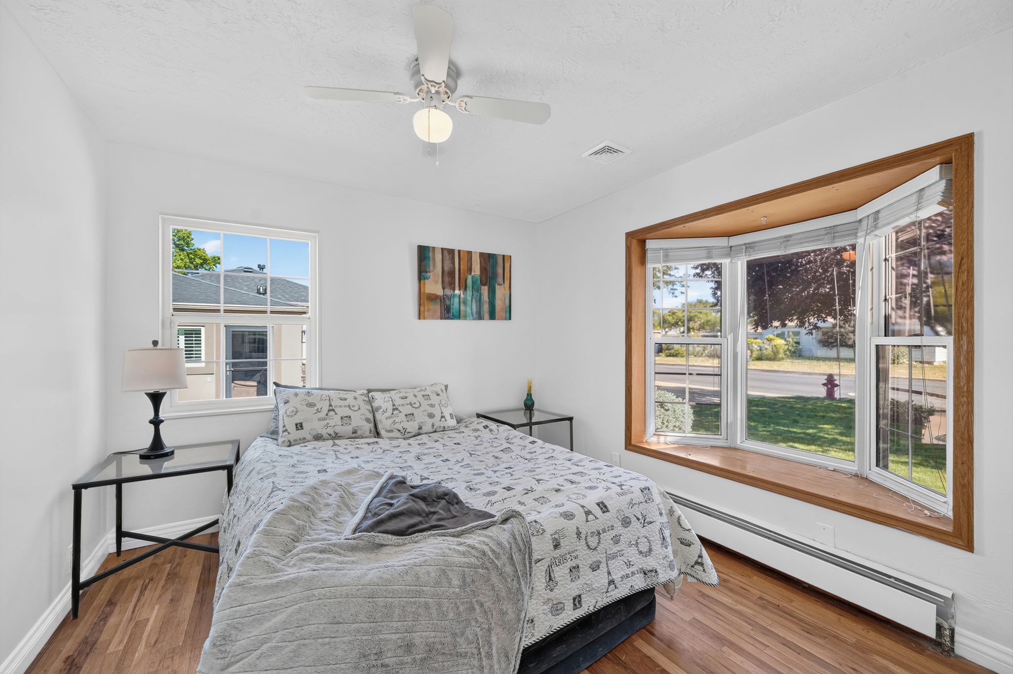 Bedroom featuring wood-finish flooring, a ceiling fan with light, and a prominent bay window with a wood-trimmed frame