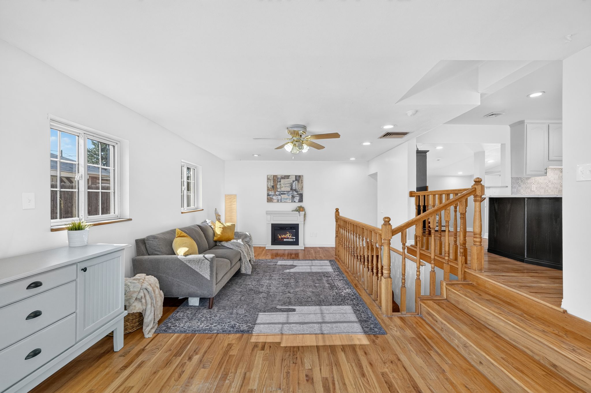 Living area featuring wood-finish flooring, a white fireplace with mantel, and a ceiling fan