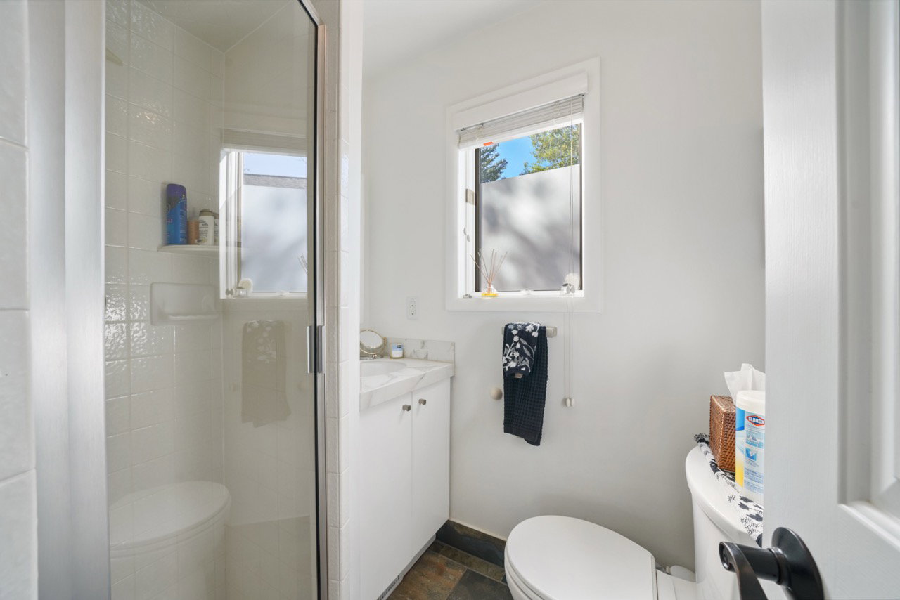 Contemporary bathroom featuring a glass-enclosed shower with white subway tile, a vanity with a stone-finish countertop, and dark-finish flooring