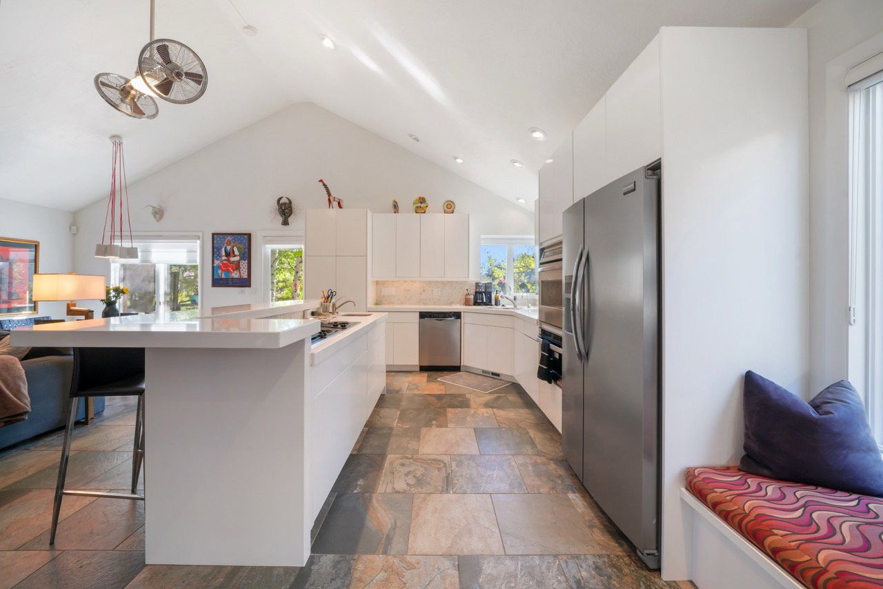 Open-concept kitchen featuring vaulted ceilings, a large island with integrated cooktop, stainless steel appliances, and multi-toned slate flooring