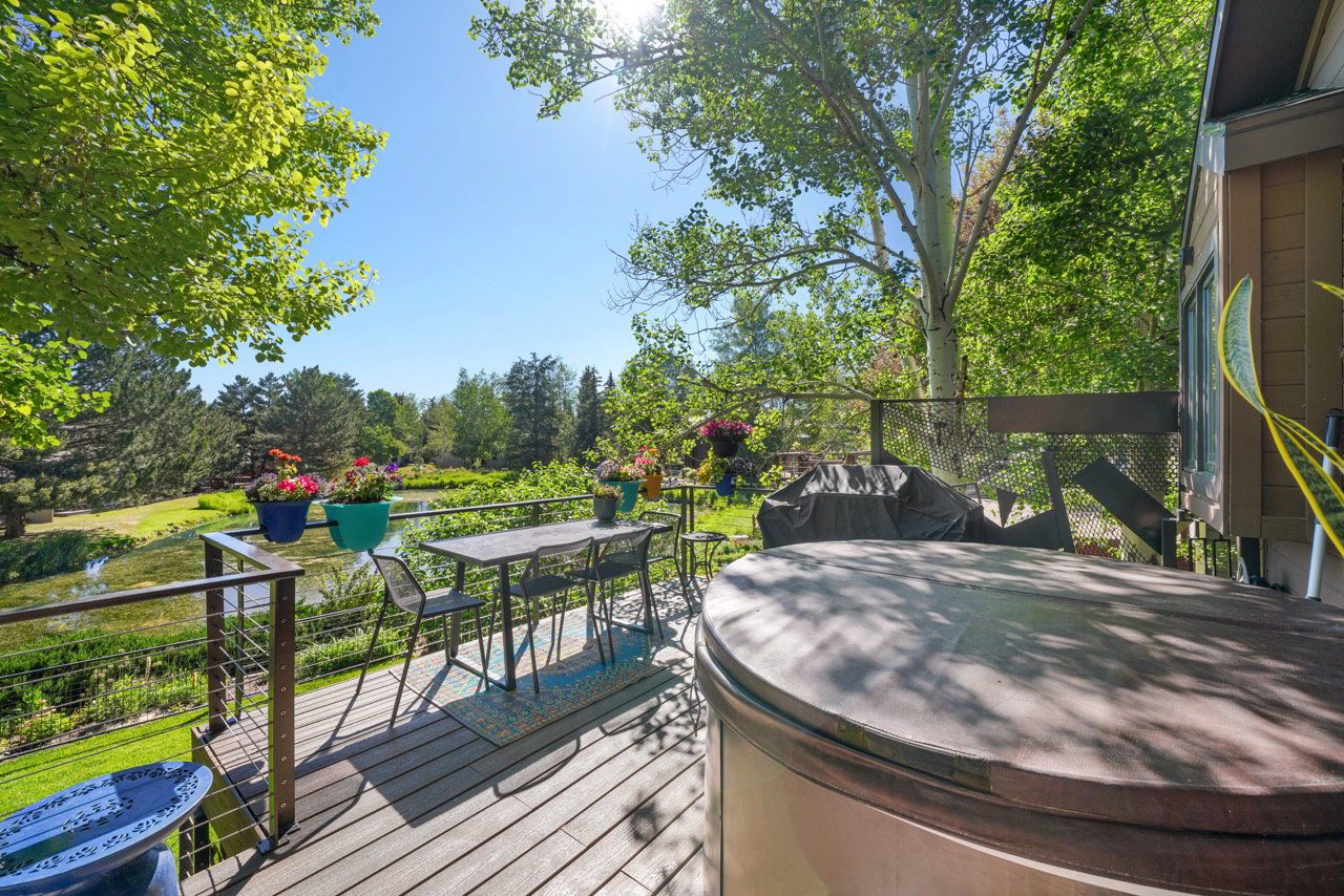 Outdoor composite deck with cable railing overlooking a water feature, mature trees, and landscaping