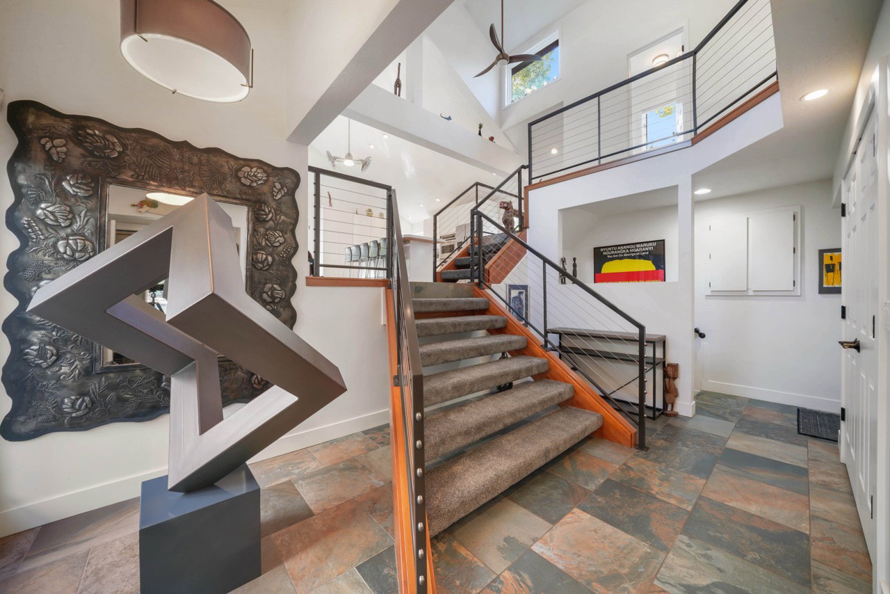 Multi-level entryway featuring slate-style tile flooring, a carpeted staircase with wood treads and metal cable railings, a vaulted ceiling, and transom windows