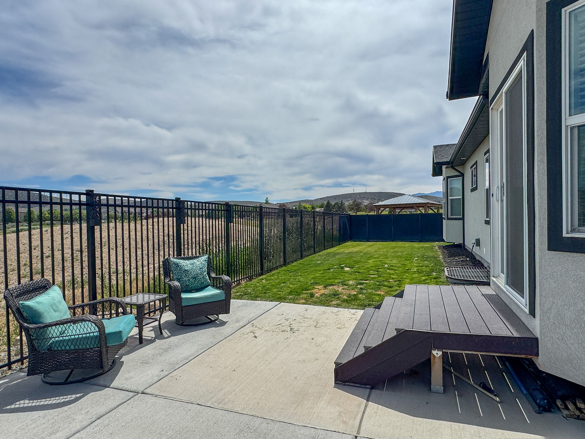 Backyard patio featuring a concrete surface, black metal fencing, a small lawn area, and a composite deck with stairs