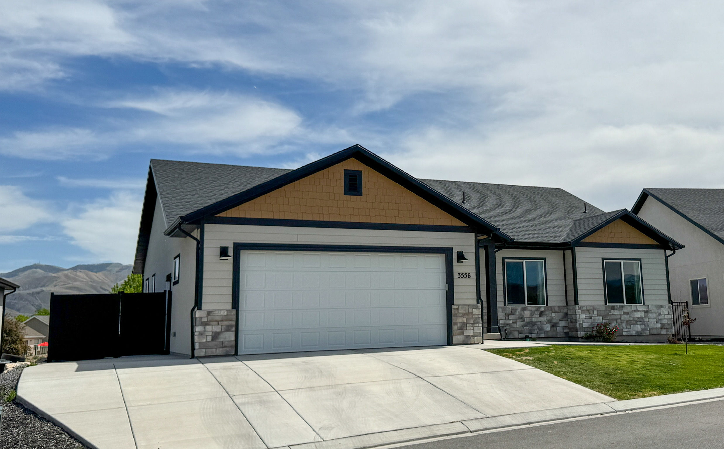 Contemporary single-story residence featuring a two-car garage, stone veneer accents, and a dark asphalt shingle roof