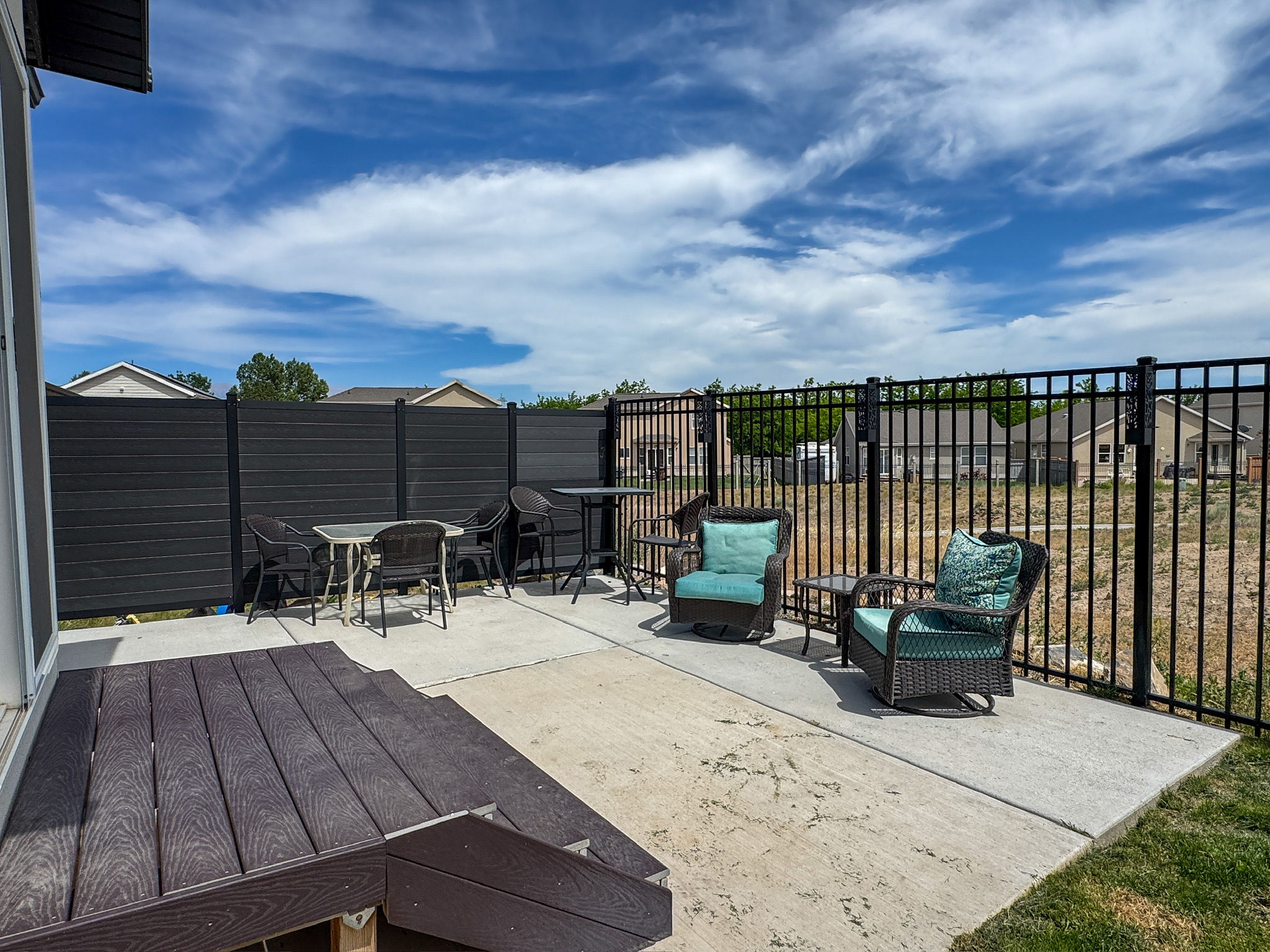 Outdoor concrete patio featuring a black metal fence and a dark composite deck with steps