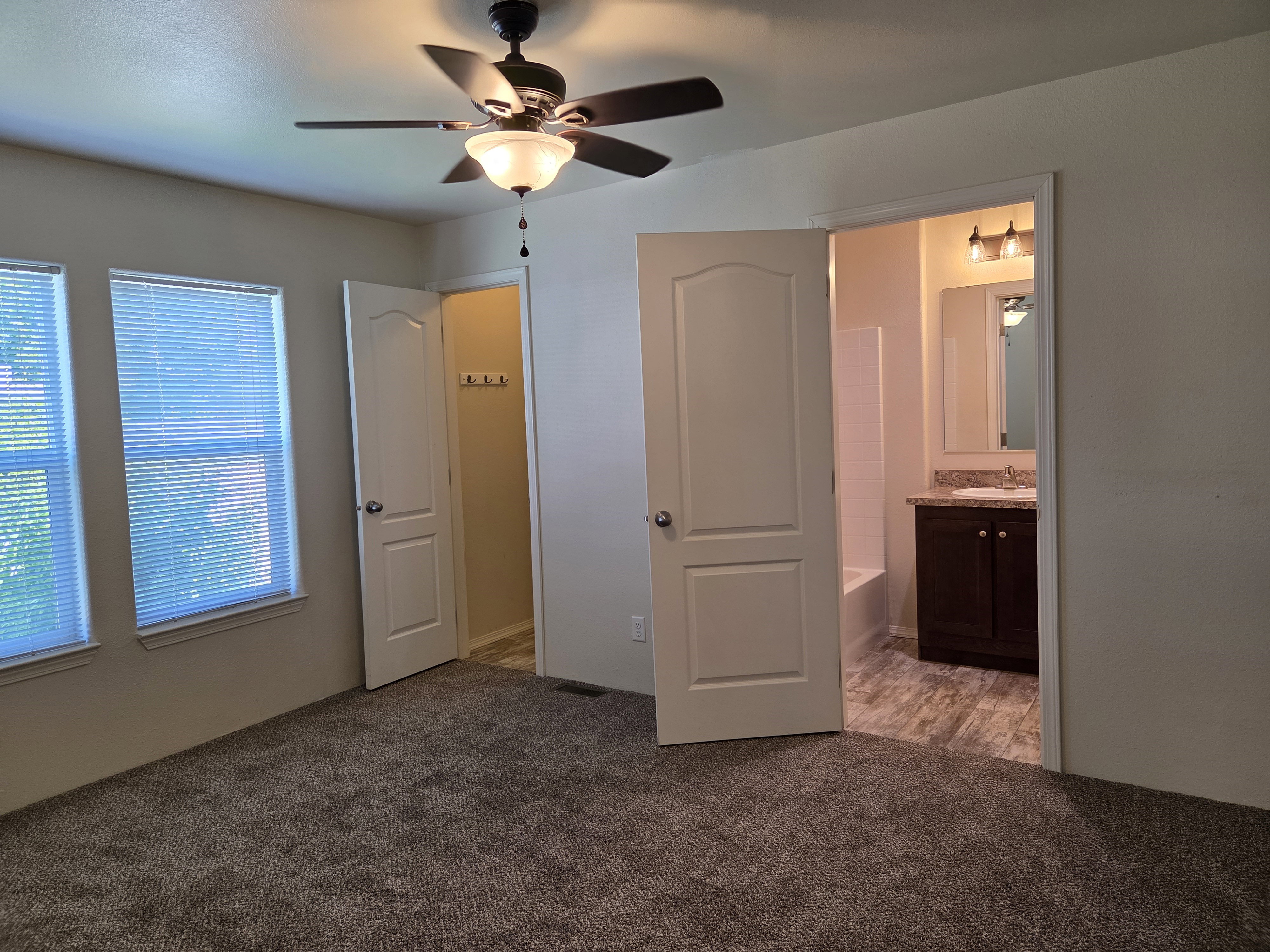 Bedroom featuring carpeting, dual windows, a ceiling fan, and direct access to a full bathroom