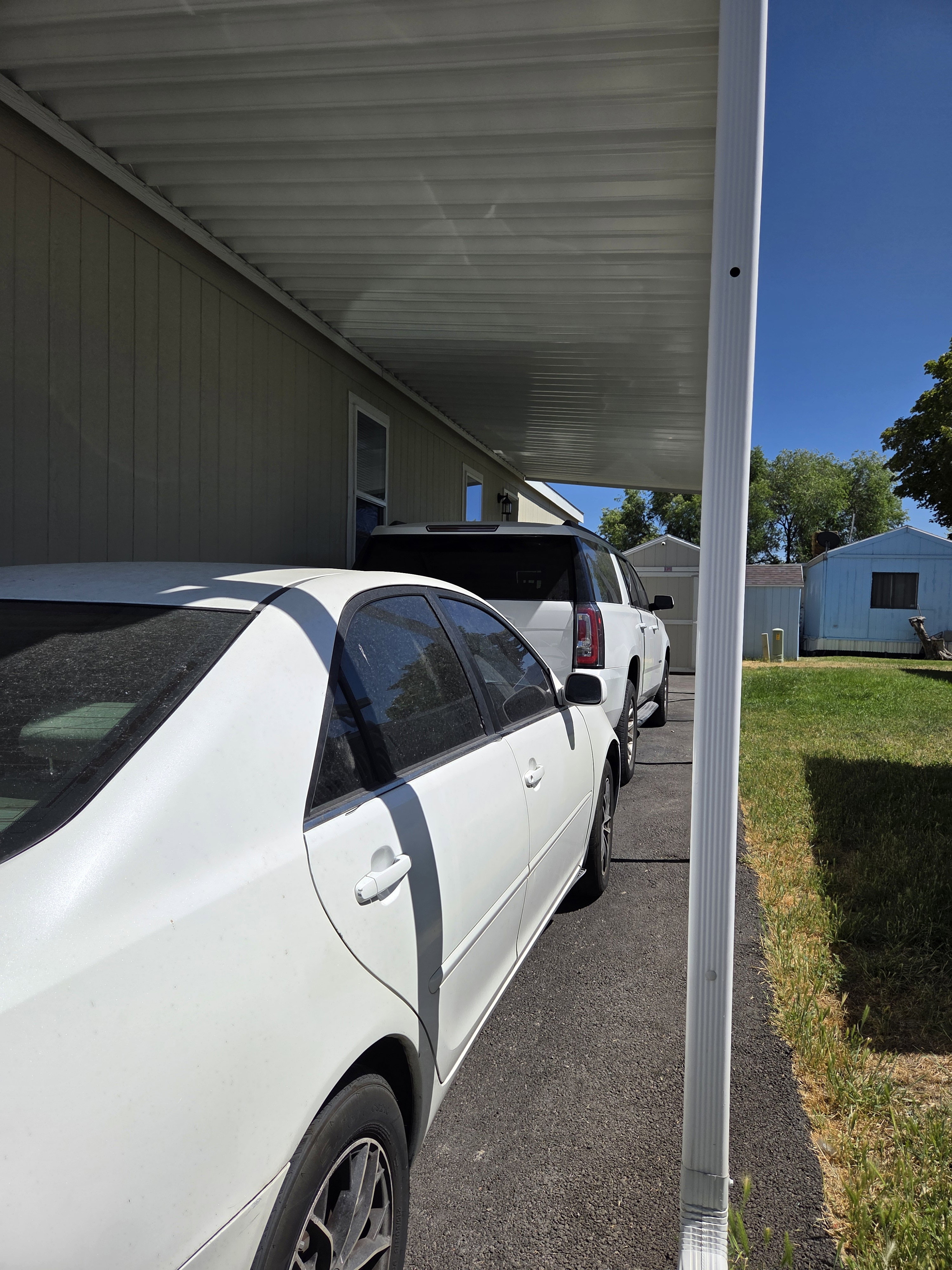 Carport with a corrugated metal roof providing covered parking, paved driveway, light-colored siding