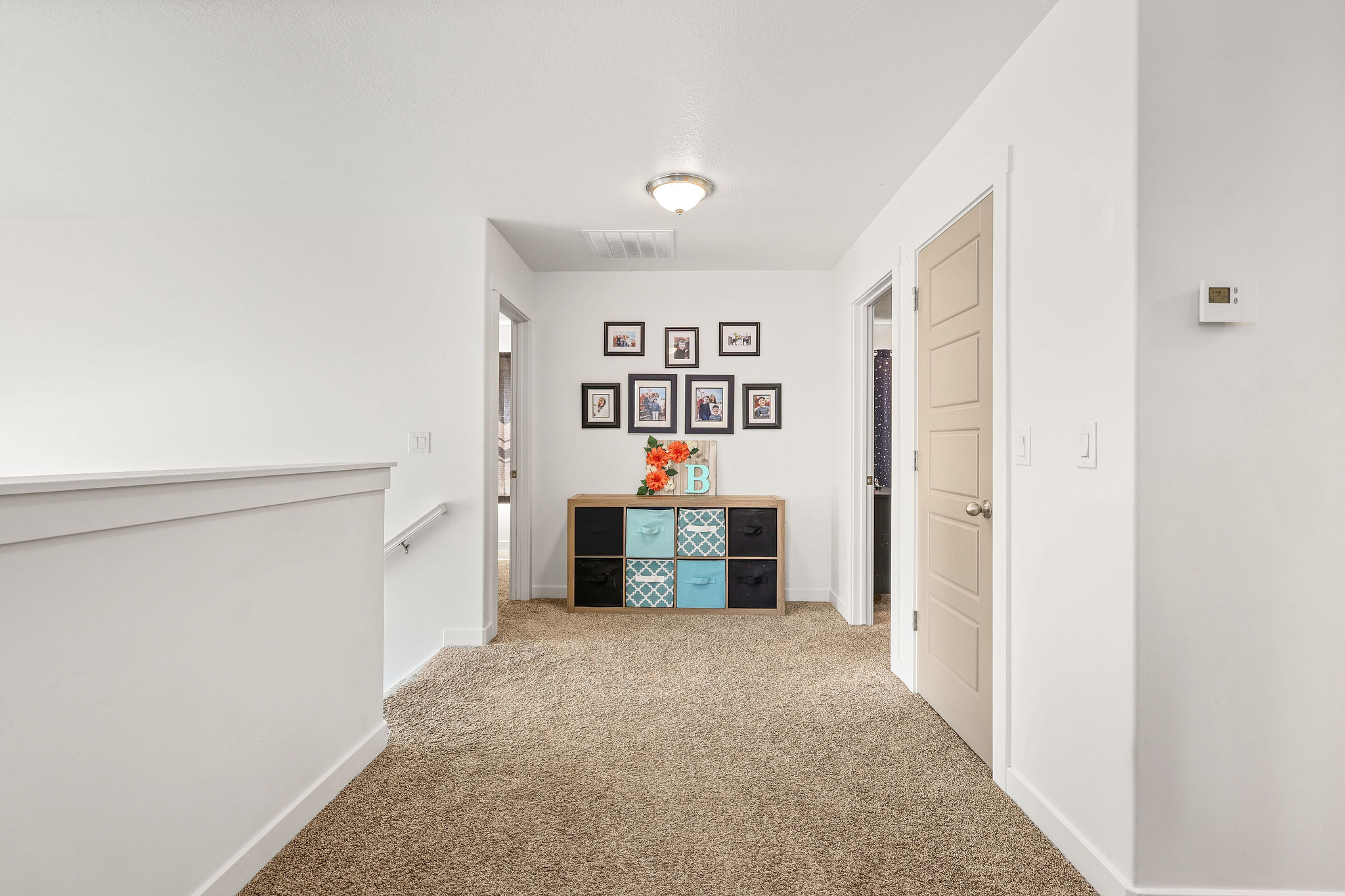 Carpeted hallway featuring white walls, a white railing with a metal handrail, a flush-mount ceiling light, and panel doors