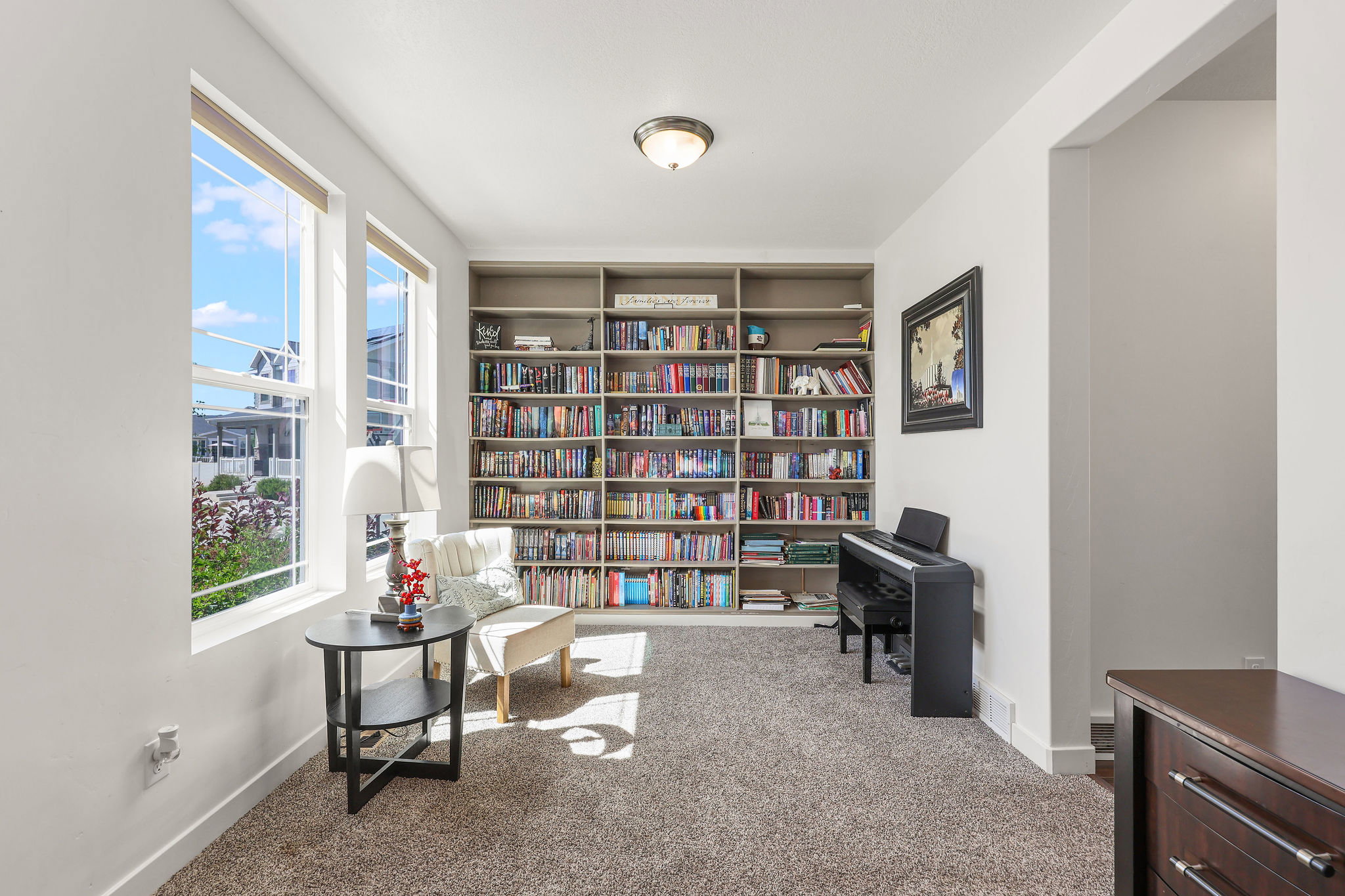 Carpeted room featuring a full wall of built-in shelving, two large windows, an overhead semi-flush mount light fixture, and white baseboards