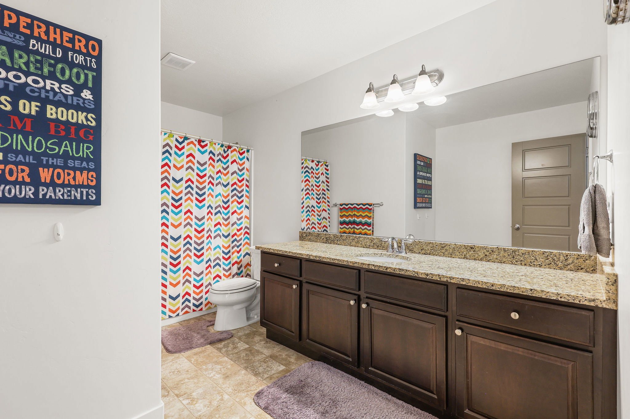Full bathroom featuring a dark wood-finish vanity with a light-colored countertop, a single sink, and a large wall-mounted mirror