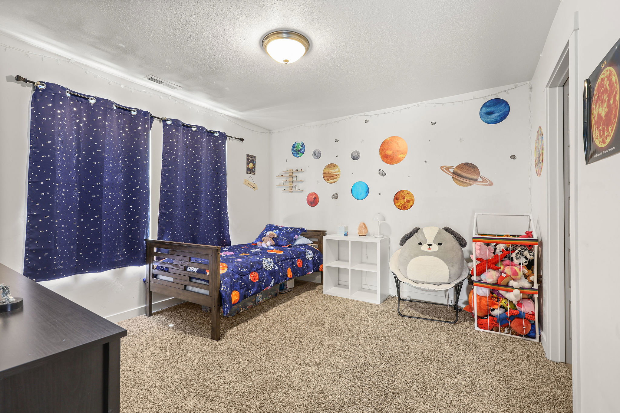 Carpeted bedroom with a wood-finish bed frame, white walls, and a ceiling-mounted light fixture