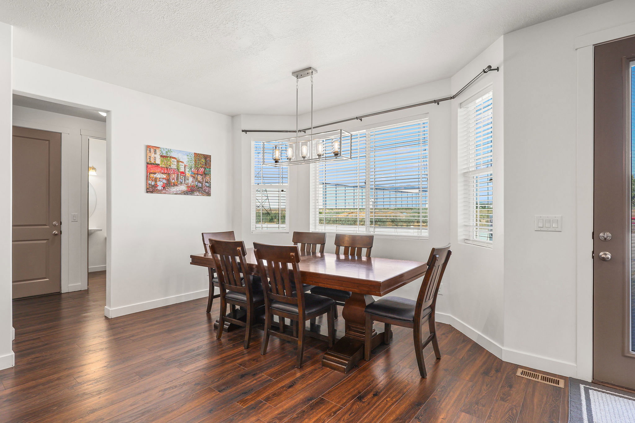 Dining area featuring wood-finish flooring, a contemporary linear chandelier, multiple windows with horizontal blinds, and a neutral color palette